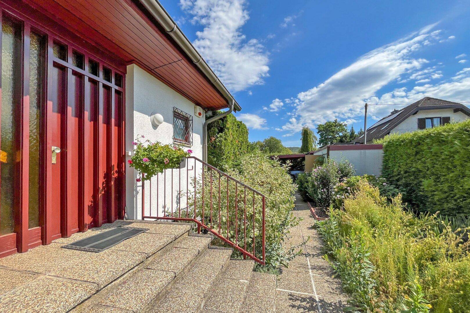 Eingangsbereich des Hauses mit roten Türen, Treppe und gepflegtem Vorgarten.