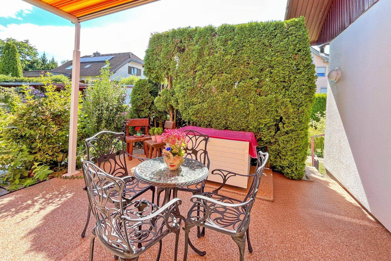 Kleiner, gemütlicher Terrassenbereich mit schmiedeeisernen Möbeln und Hecke als Sichtschutz.