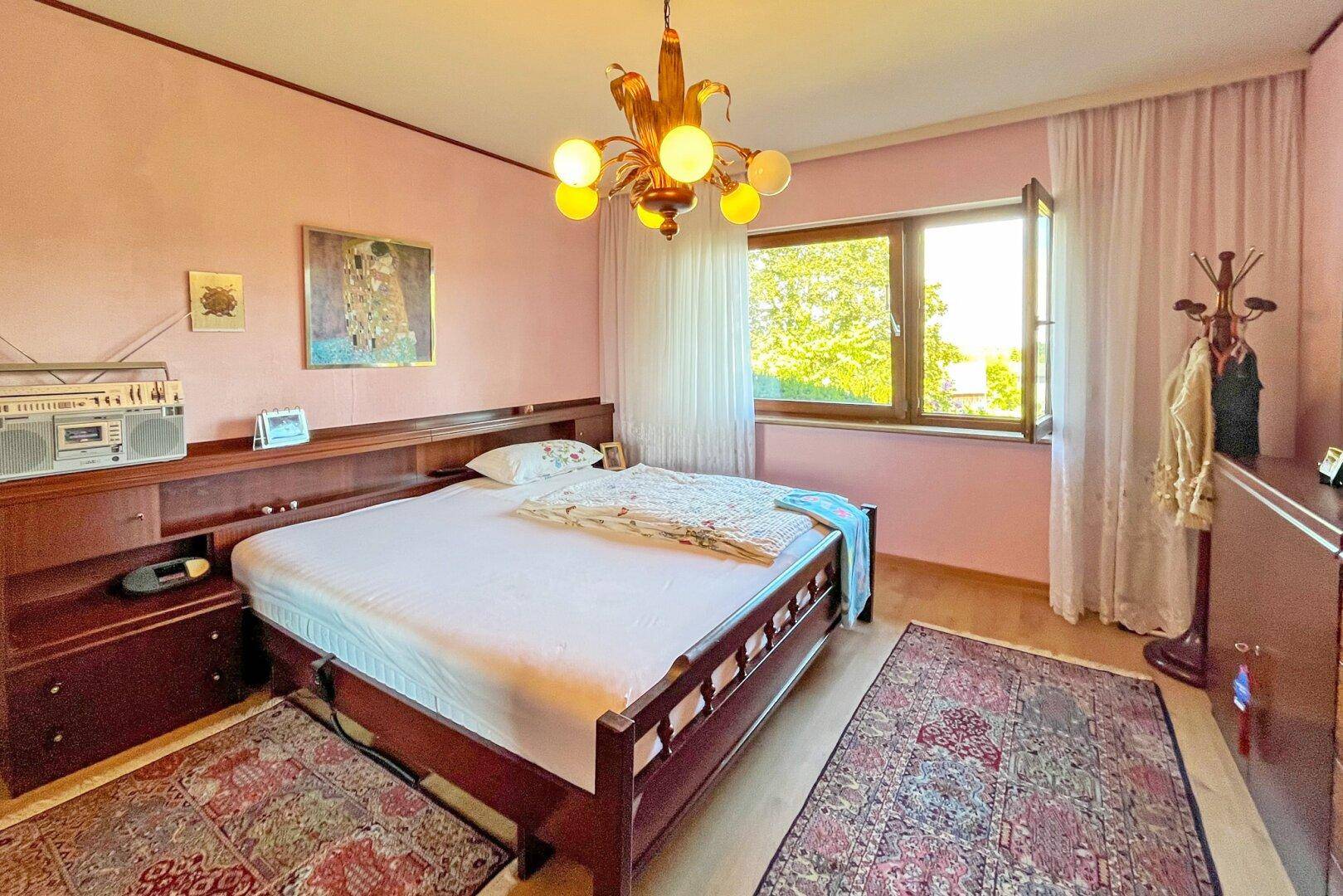 Schlafzimmer mit rosa Wänden, Doppelbett und Fenster mit Blick in die Natur.