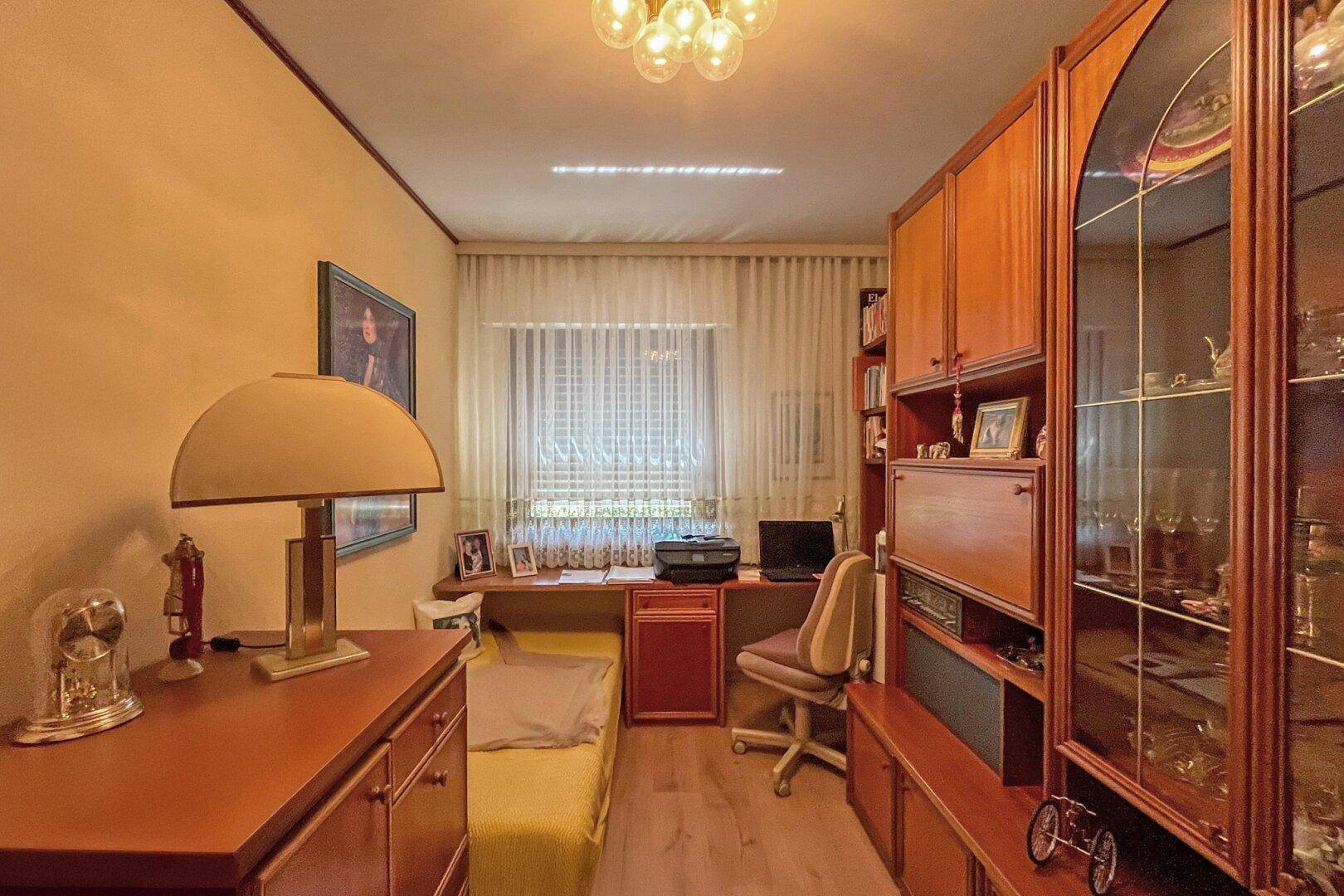 Arbeitszimmer mit Holzmöbeln, Schreibtisch und Fenster mit Vorhängen.
