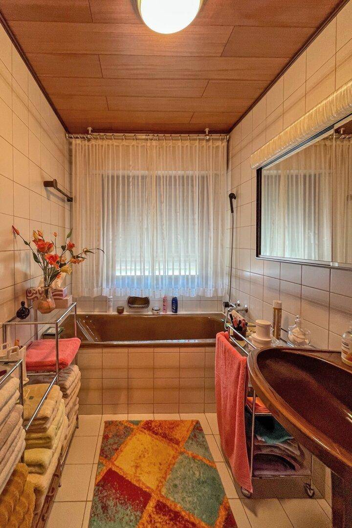 Badezimmer mit Badewanne, Fliesenwänden und Holzdecke in traditionellem Stil.