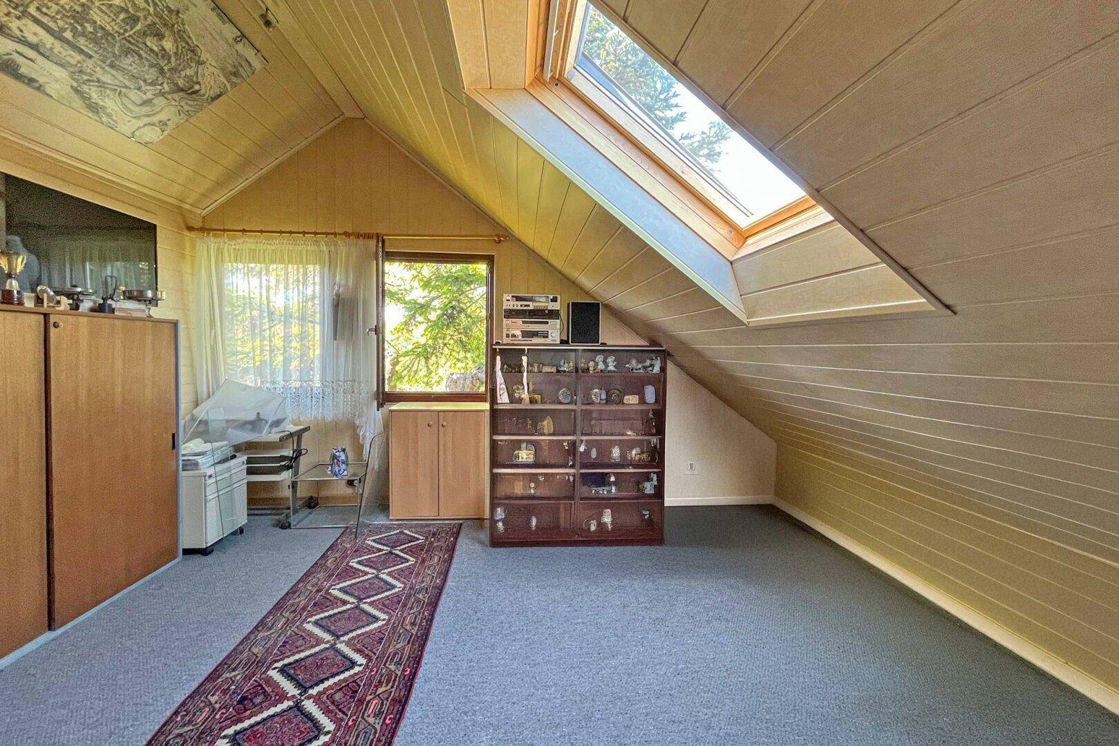 Dachgeschosszimmer mit Teppichboden, Dachschräge und Dachfenster für natürliches Licht.