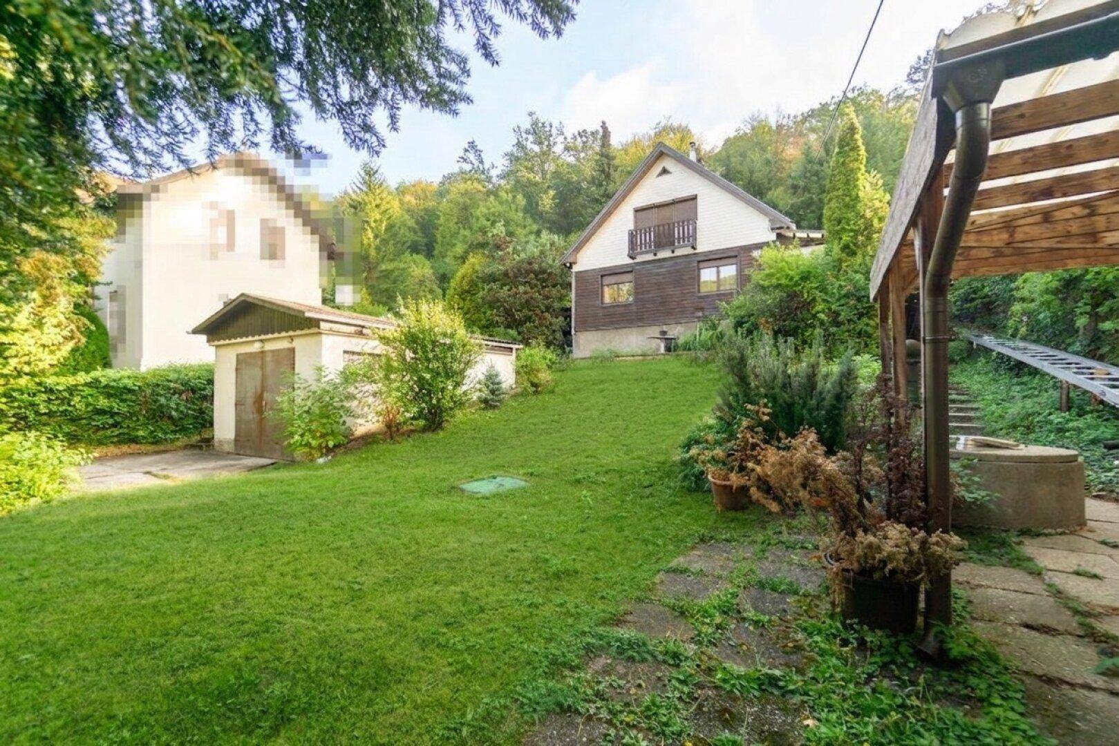 Weitläufiger Gartenbereich mit Rasenfläche, einem kleinen Schuppen und dem Haupthaus im Hintergrund.