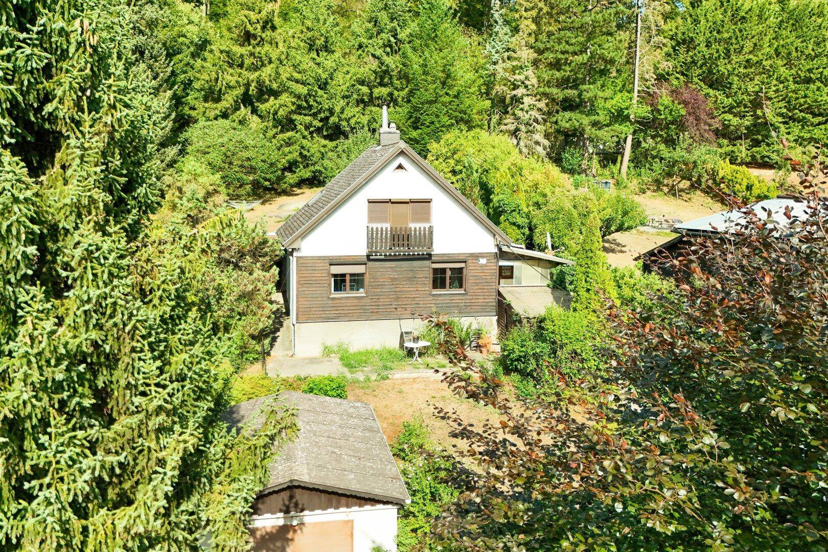 Das Haus ist von üppigem Grün umgeben und bietet einen Balkon mit Blick auf die bewaldete Hügellandschaft.