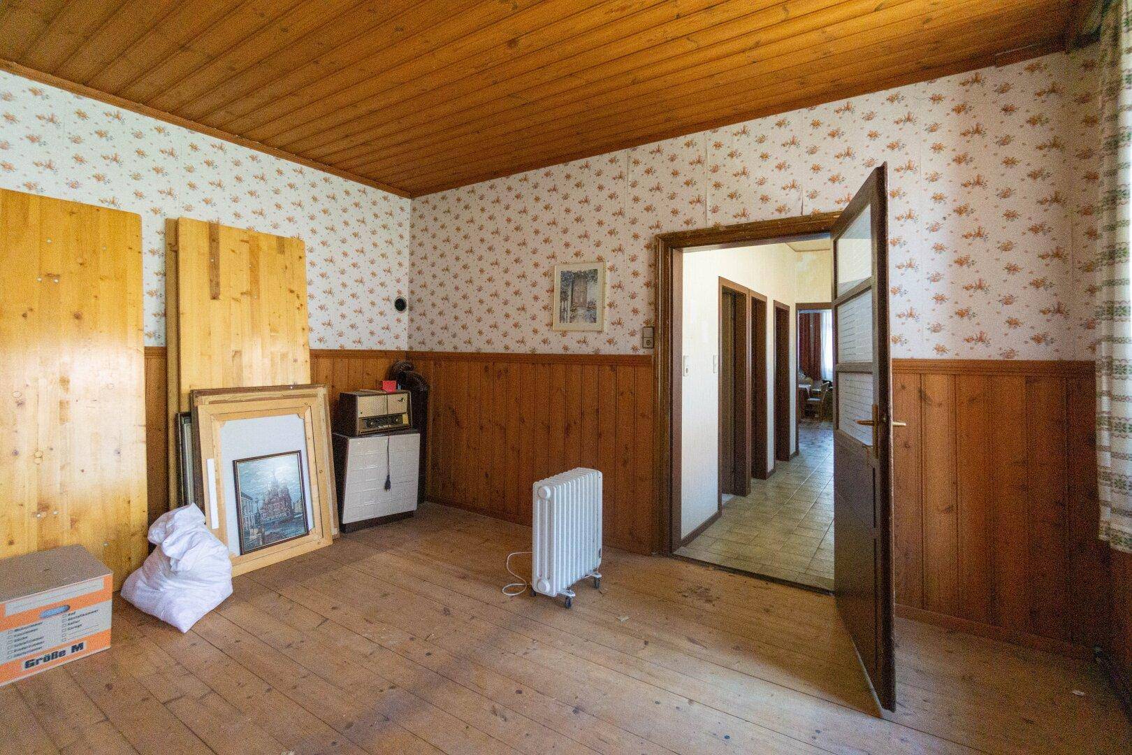 Geräumiges Zimmer mit Holzvertäfelung, gemusterter Tapete und Holzboden, bereit zur Renovierung.
