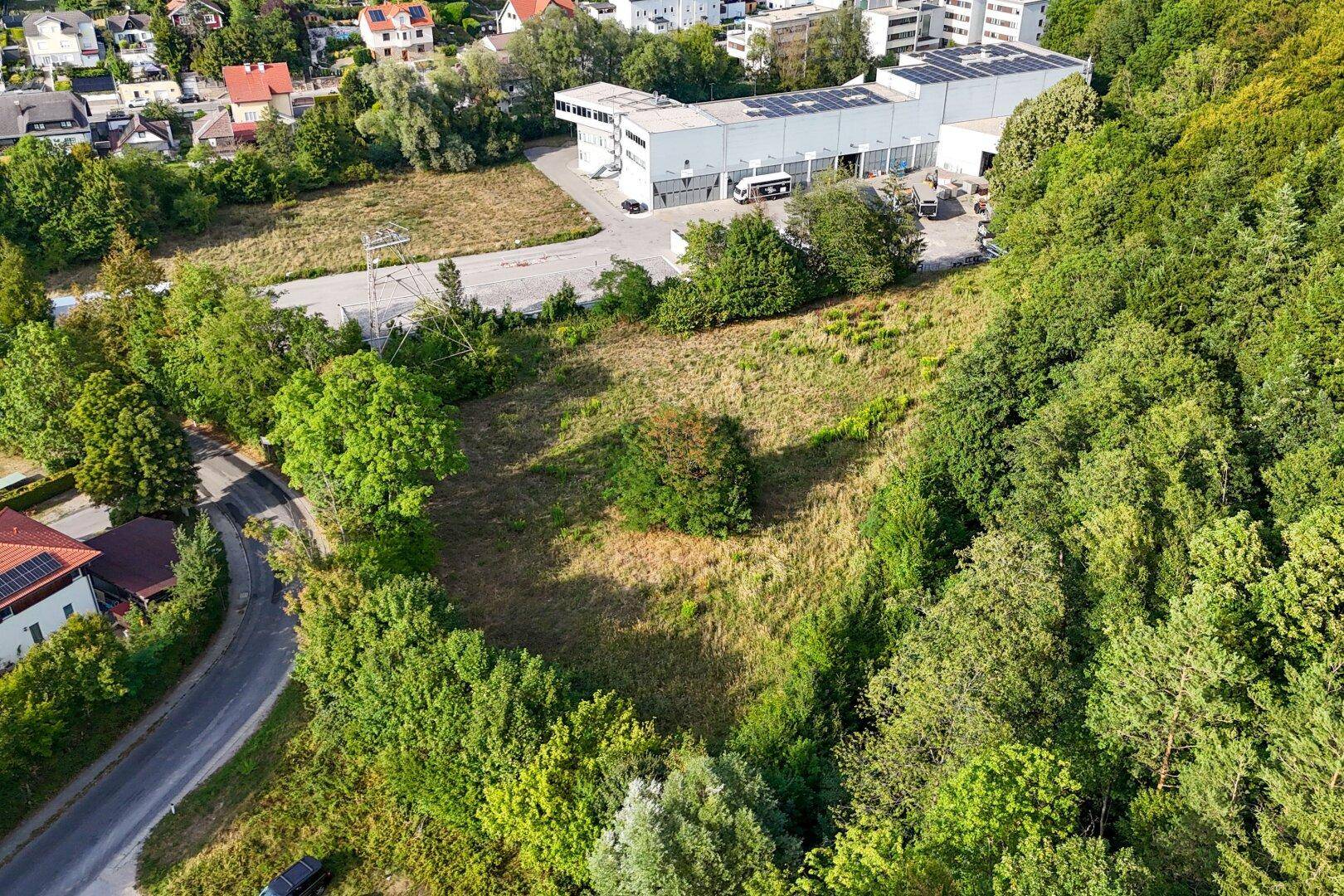 Weitläufige Luftaufnahme eines unbebauten Grundstücks, umgeben von Wald, Gewerbe und Wohnbebauung.