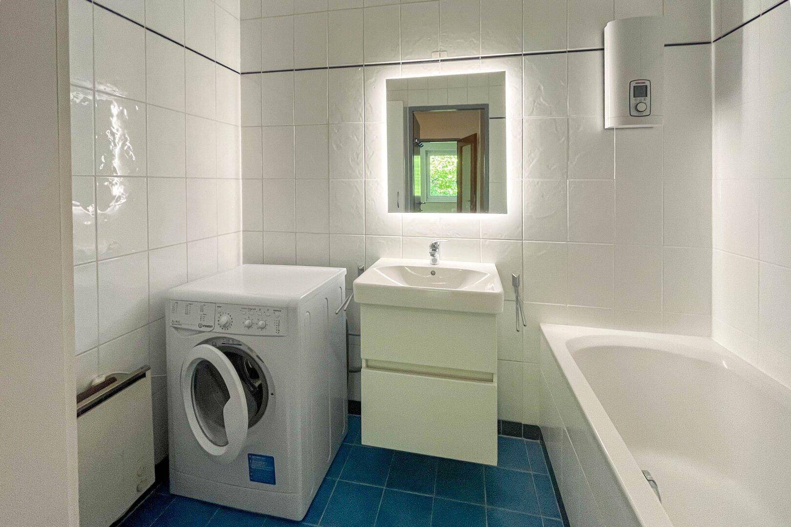 Funktionales Badezimmer mit Badewanne, Waschbecken und Waschmaschine, hell gefliest.