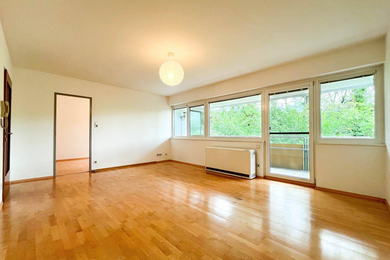 Helles Wohnzimmer mit Parkettboden, großen Fenstern und Zugang zum Balkon.