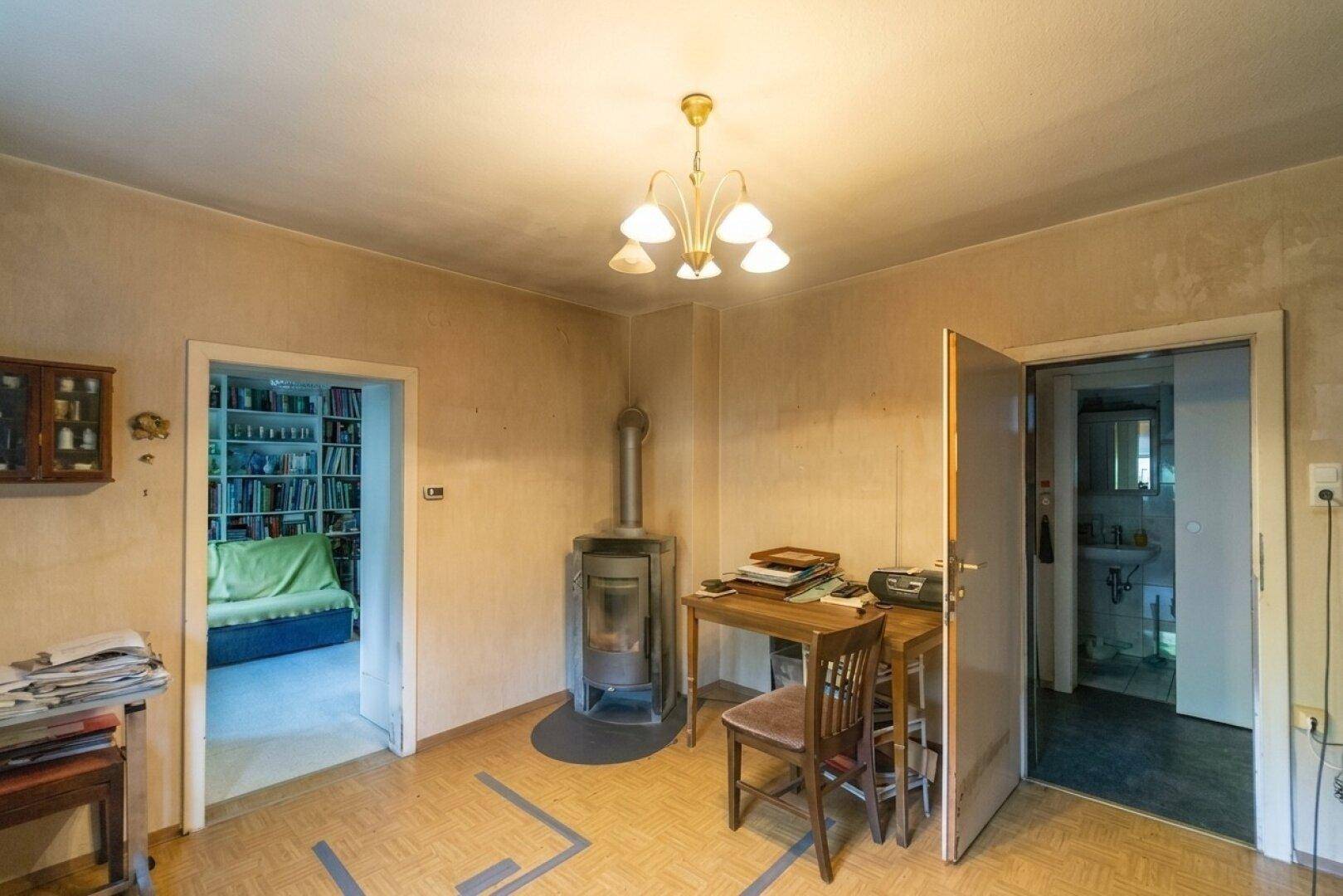 Wohnraum mit einem Holzofen als Heizquelle und Zugang zu weiteren Zimmern, mit einfacher Einrichtung.