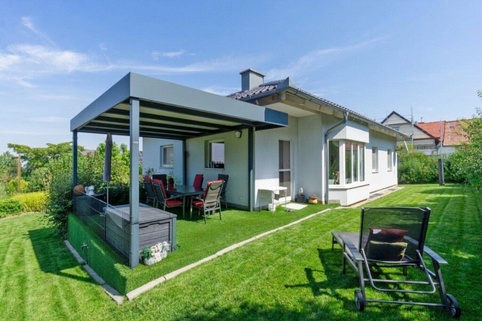 Überdachte Terrasse mit Kunstrasen und Gartenmöbeln, umgeben von einem gepflegten Rasenbereich.