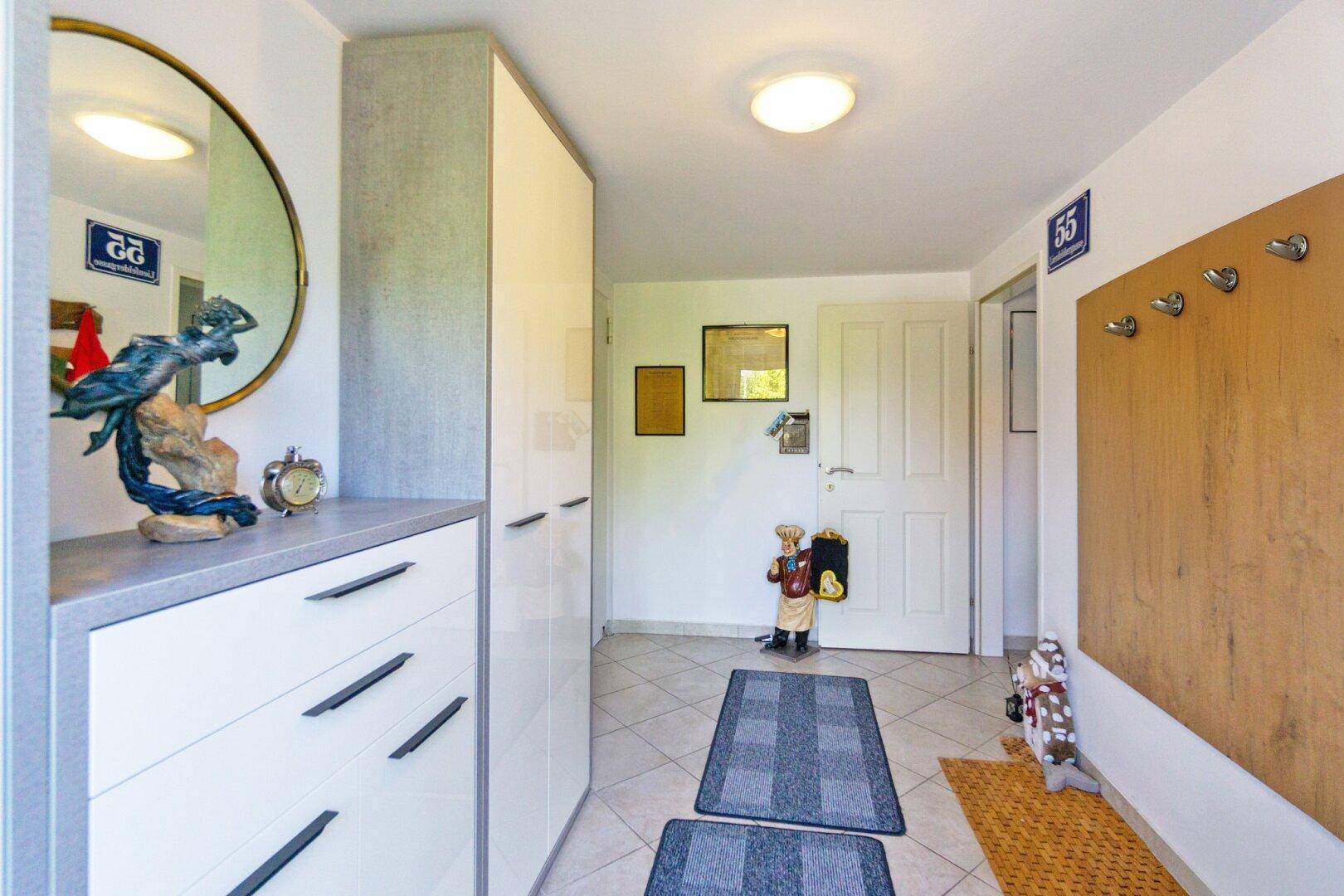 Heller Eingangsbereich mit Fliesenboden, Garderobe und einem großen runden Spiegel.
