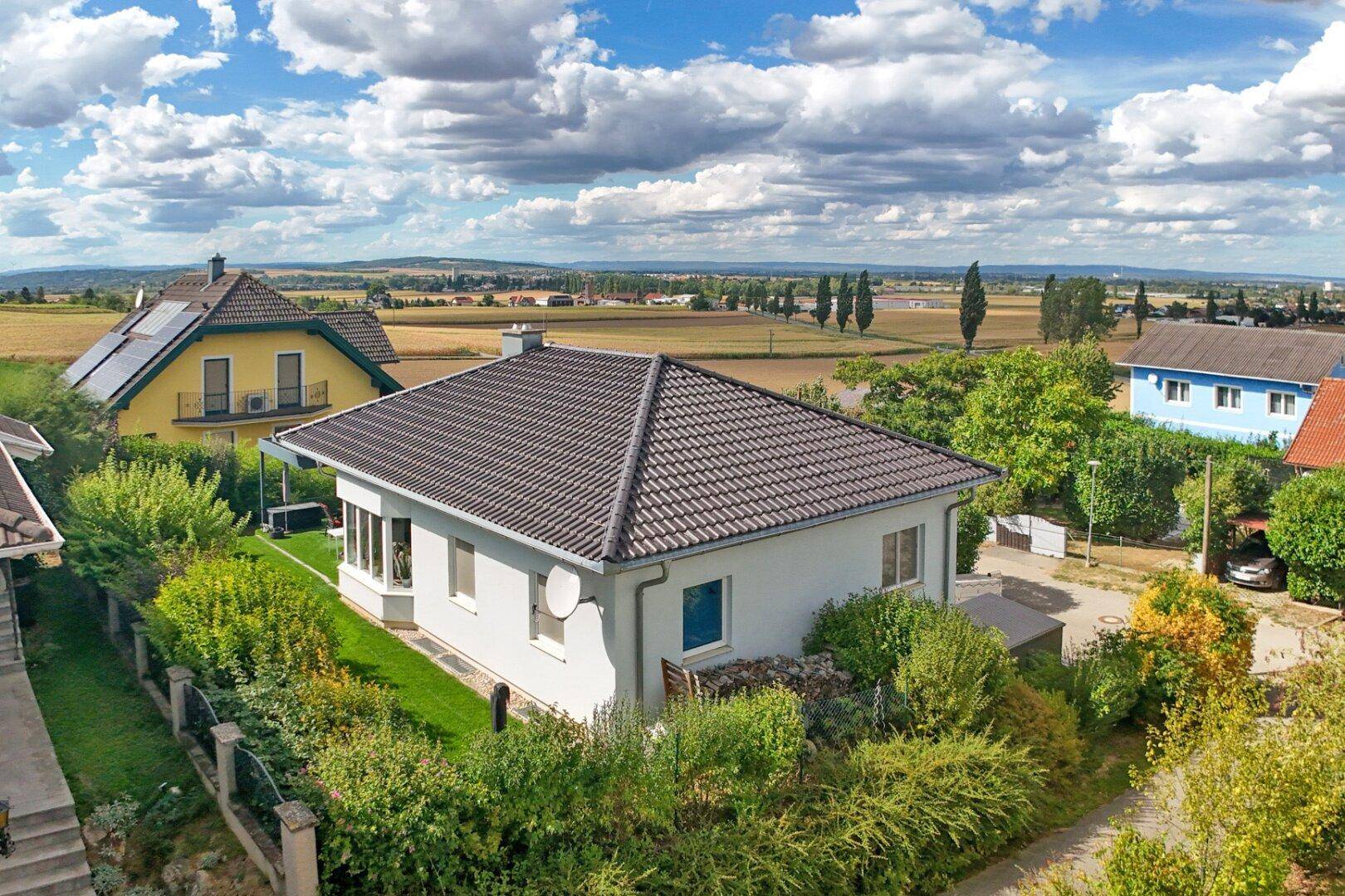 Luftaufnahme des Einfamilienhauses mit Satteldach und umliegender ländlicher Landschaft unter bewölktem Himmel.