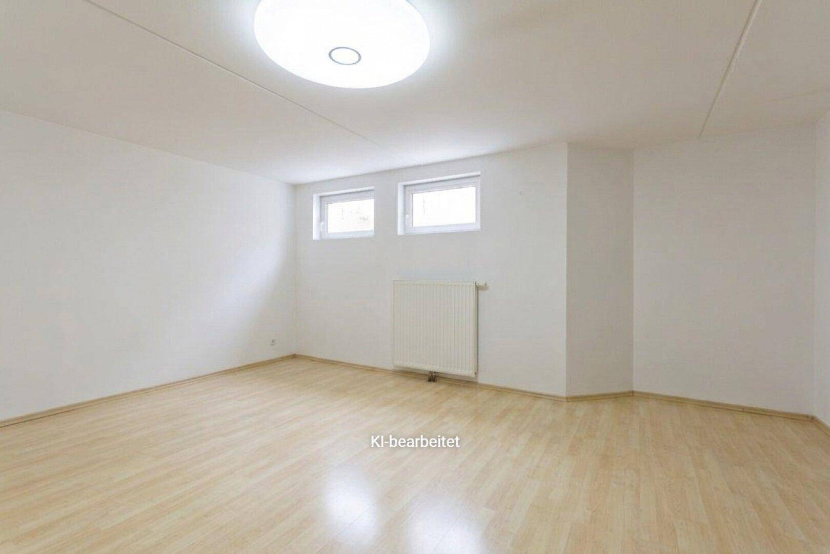 Leeres Zimmer mit hellem Laminatboden, zwei Fenstern und einem Heizkörper.