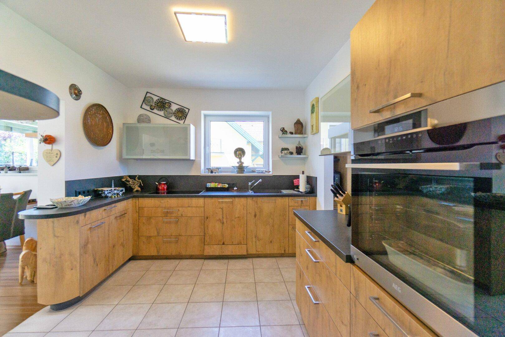 Moderne Holzküche mit dunkler Arbeitsplatte, integrierten Geräten und Fliesenboden.