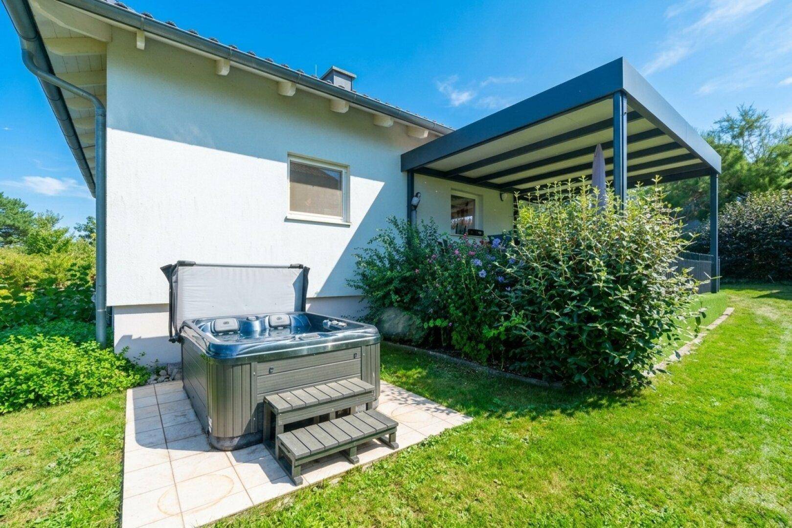 Whirlpool im Gartenbereich auf einer gepflasterten Fläche neben dem Haus.