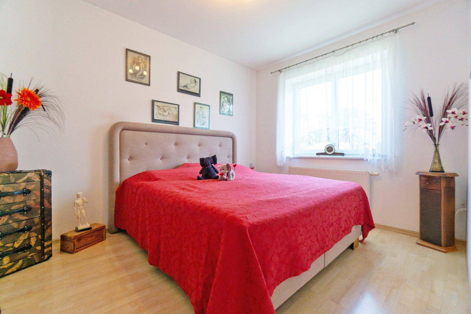Helles Schlafzimmer mit Laminatboden, großem Bett und einem Fenster mit Vorhang.