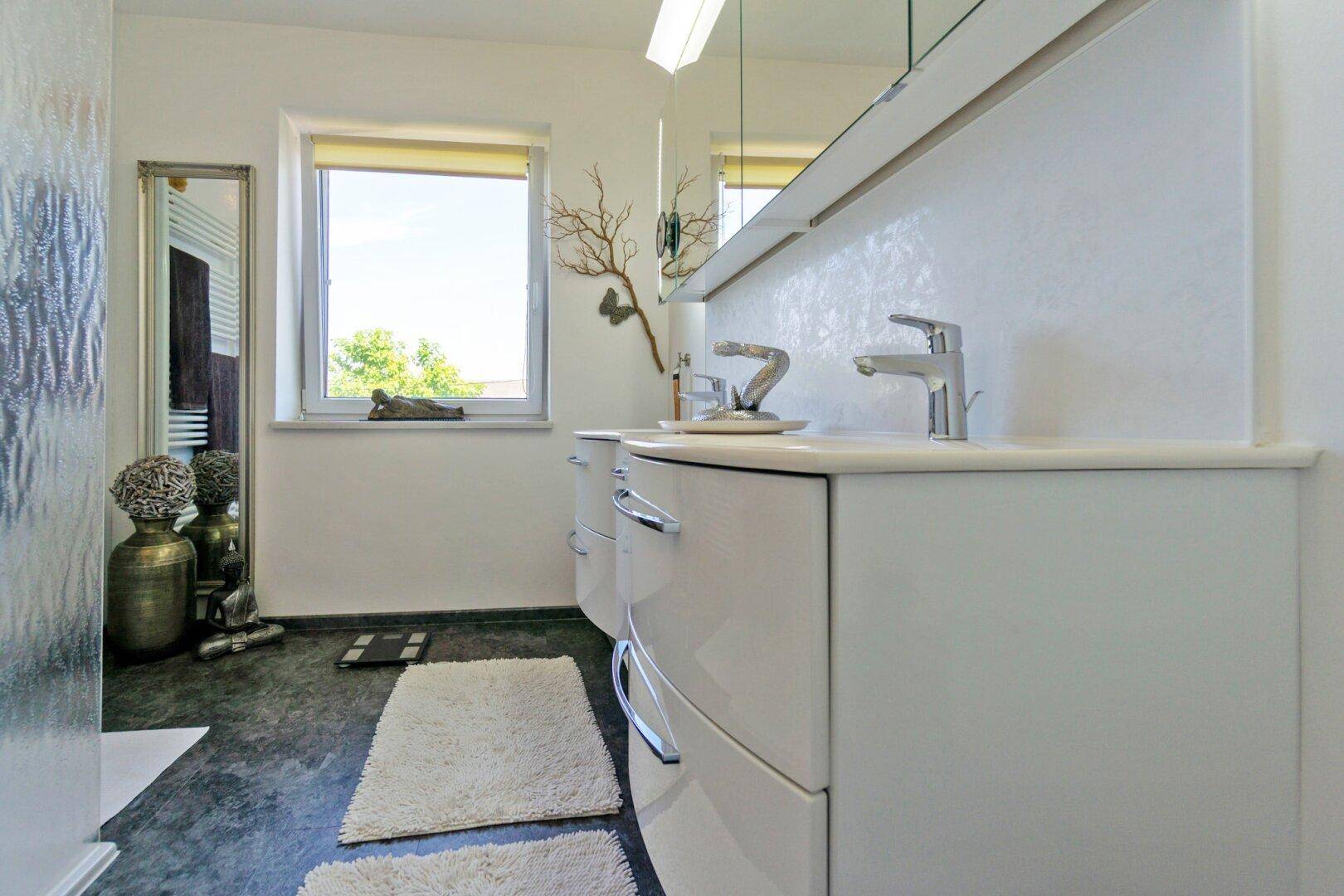 Modernes Badezimmer mit Doppelwaschbecken, großem Spiegel und Fenster.
