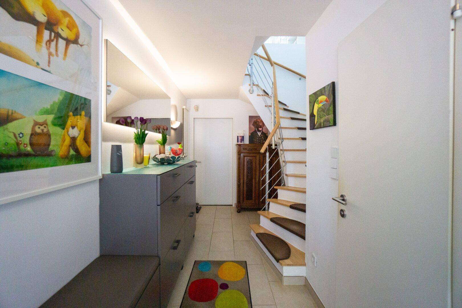 Heller Eingangsbereich mit Fliesenboden, moderner Kommode und offener Treppe.
