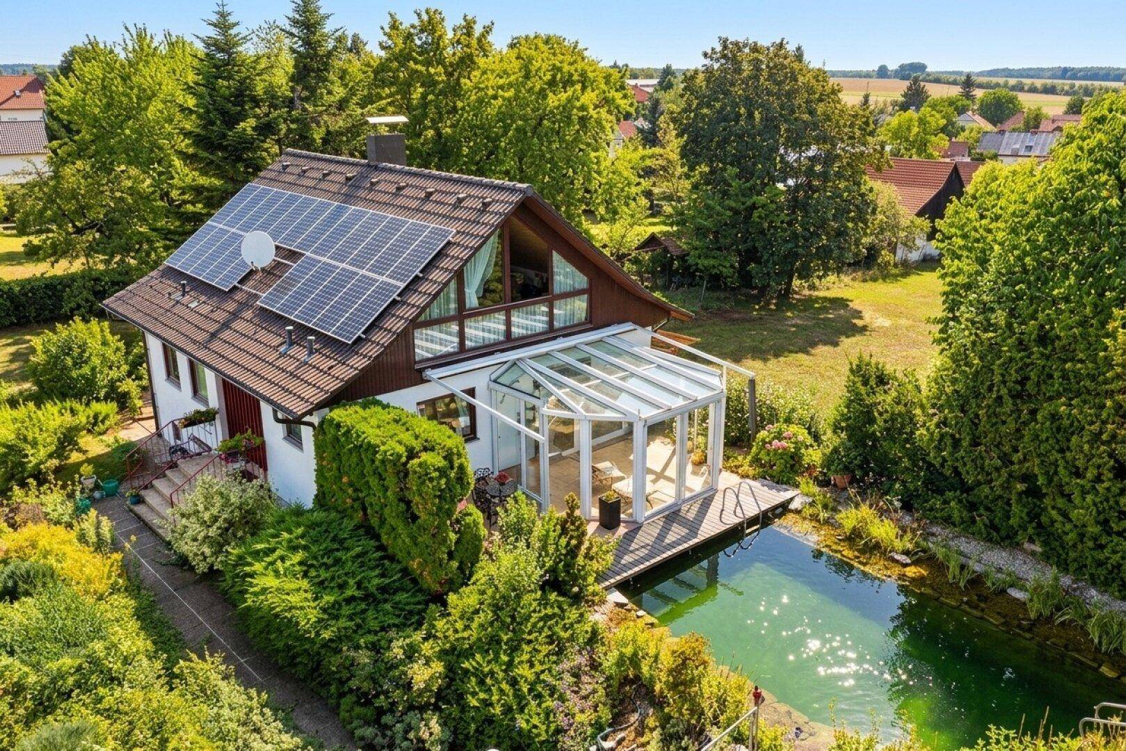 Vogelperspektive des Hauses mit Solaranlage, Wintergarten und großem Naturschwimmteich.