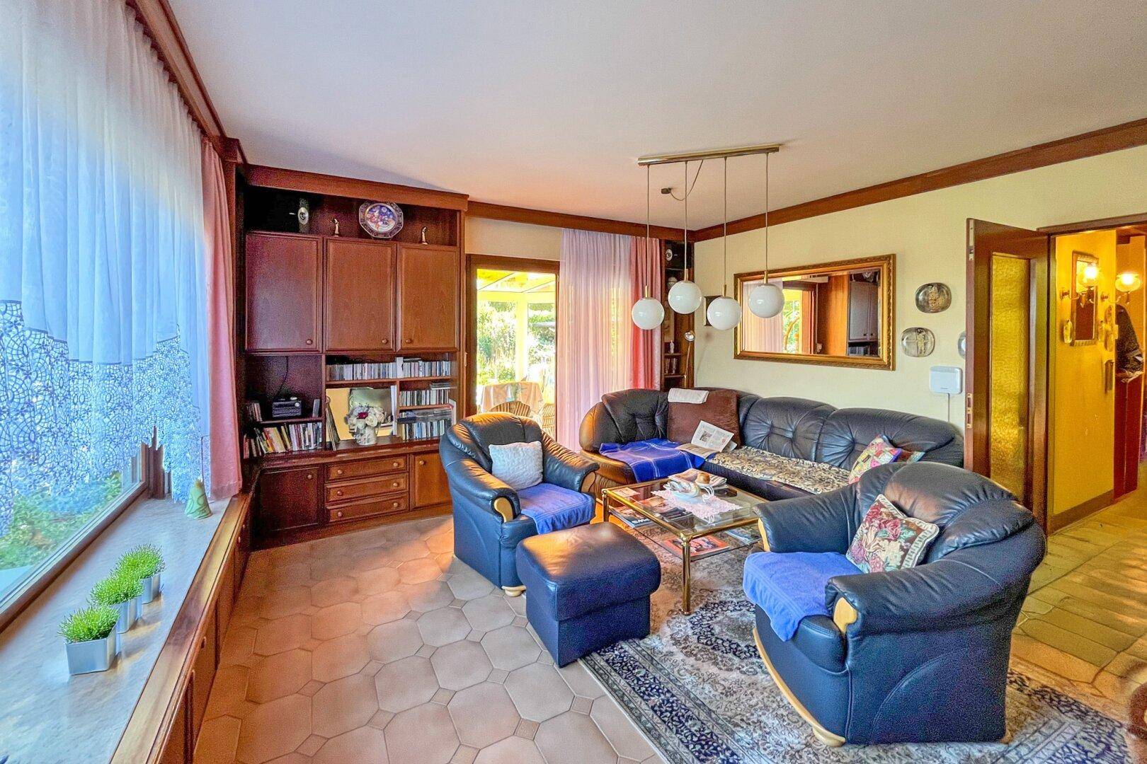 Gemütliches Wohnzimmer mit Ledersofas, Fliesenboden und Blick in den Wintergarten.