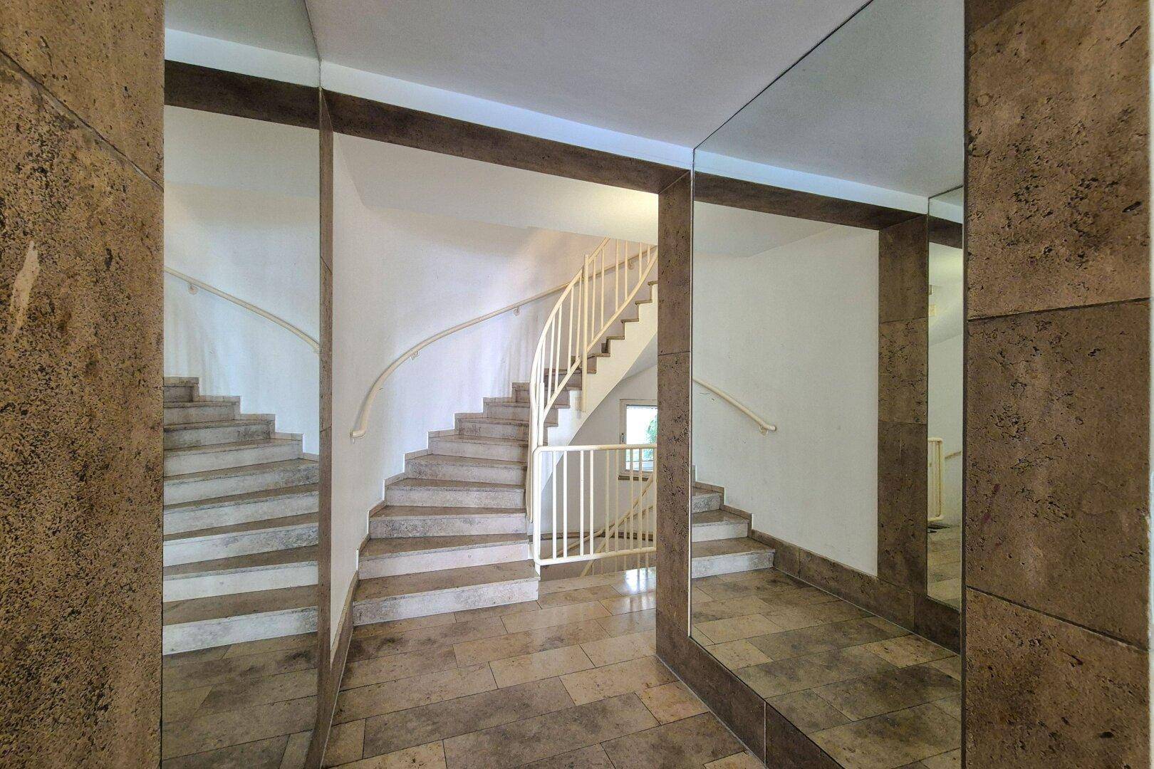 Repräsentatives Treppenhaus mit Steinfliesen, geschwungener Treppe und Spiegelflächen.