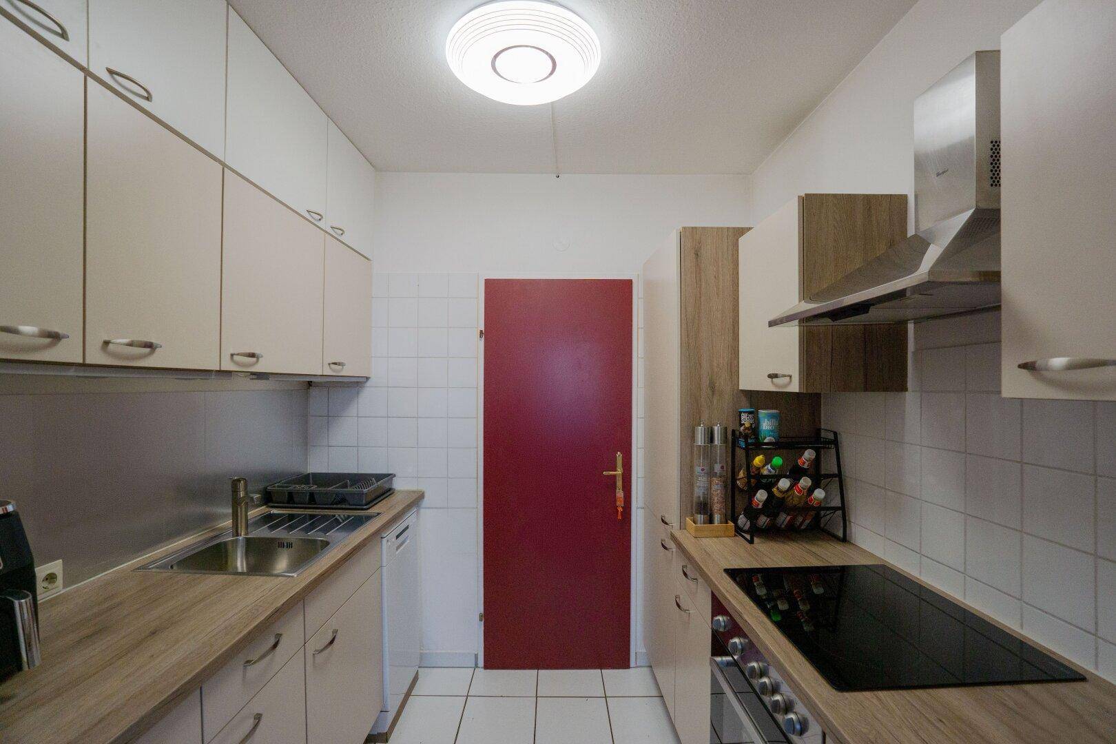 Schmale Küche mit hellen Einbauschränken, Holzoptik-Arbeitsplatte und Induktionskochfeld.