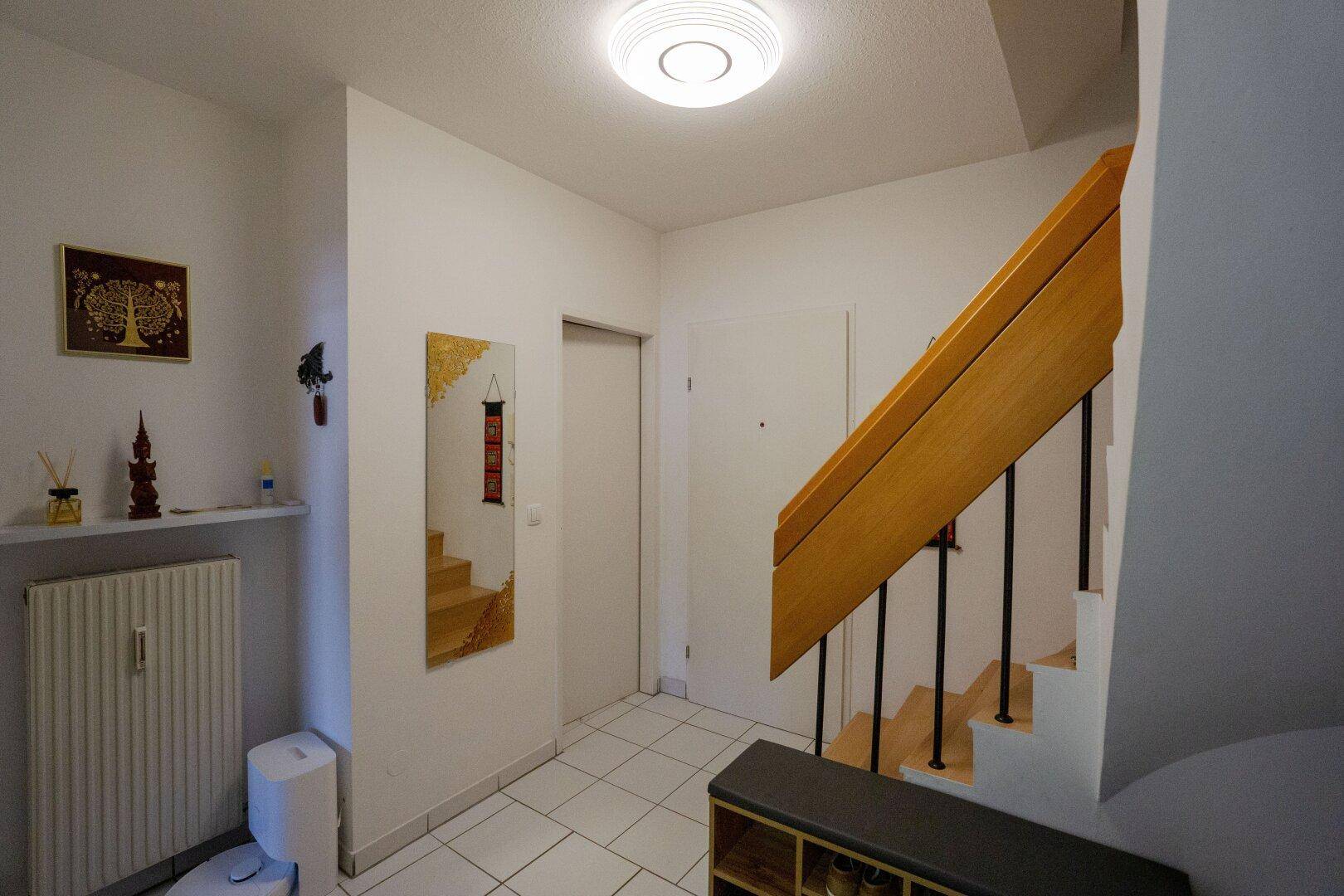 Heller Eingangsbereich mit Fliesenboden, Holztreppe und Spiegel an der Wand.