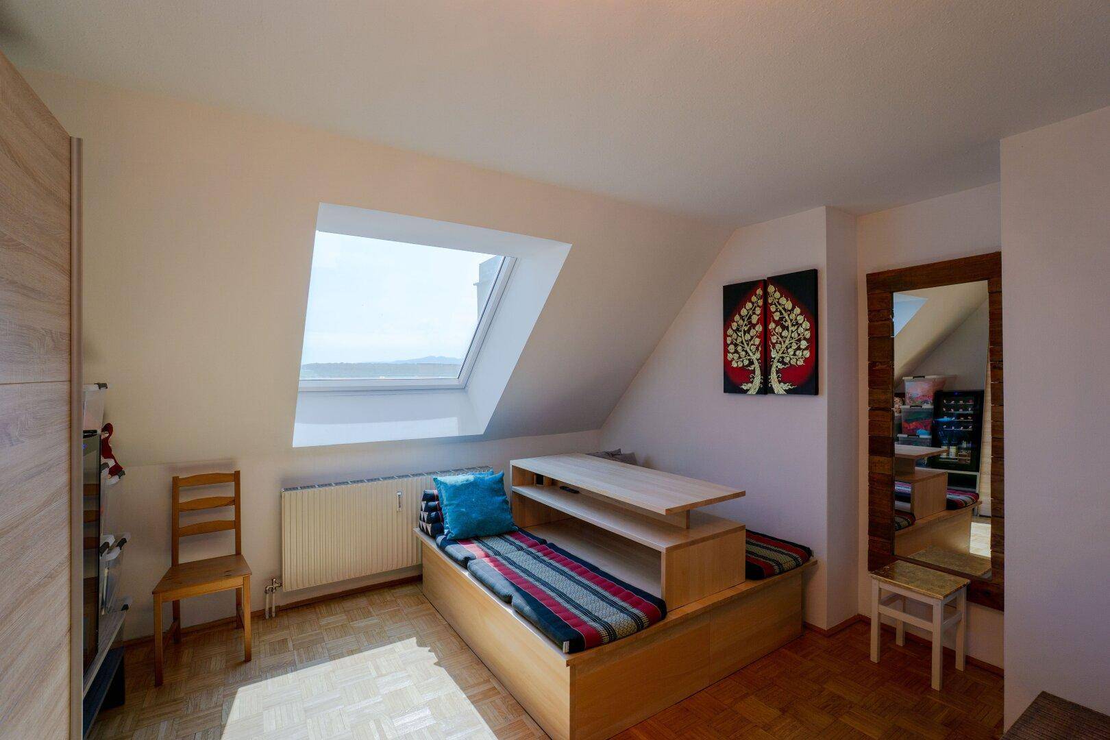 Helles Zimmer im Dachgeschoss mit Holzboden, Tagesbett und großem Dachfenster.