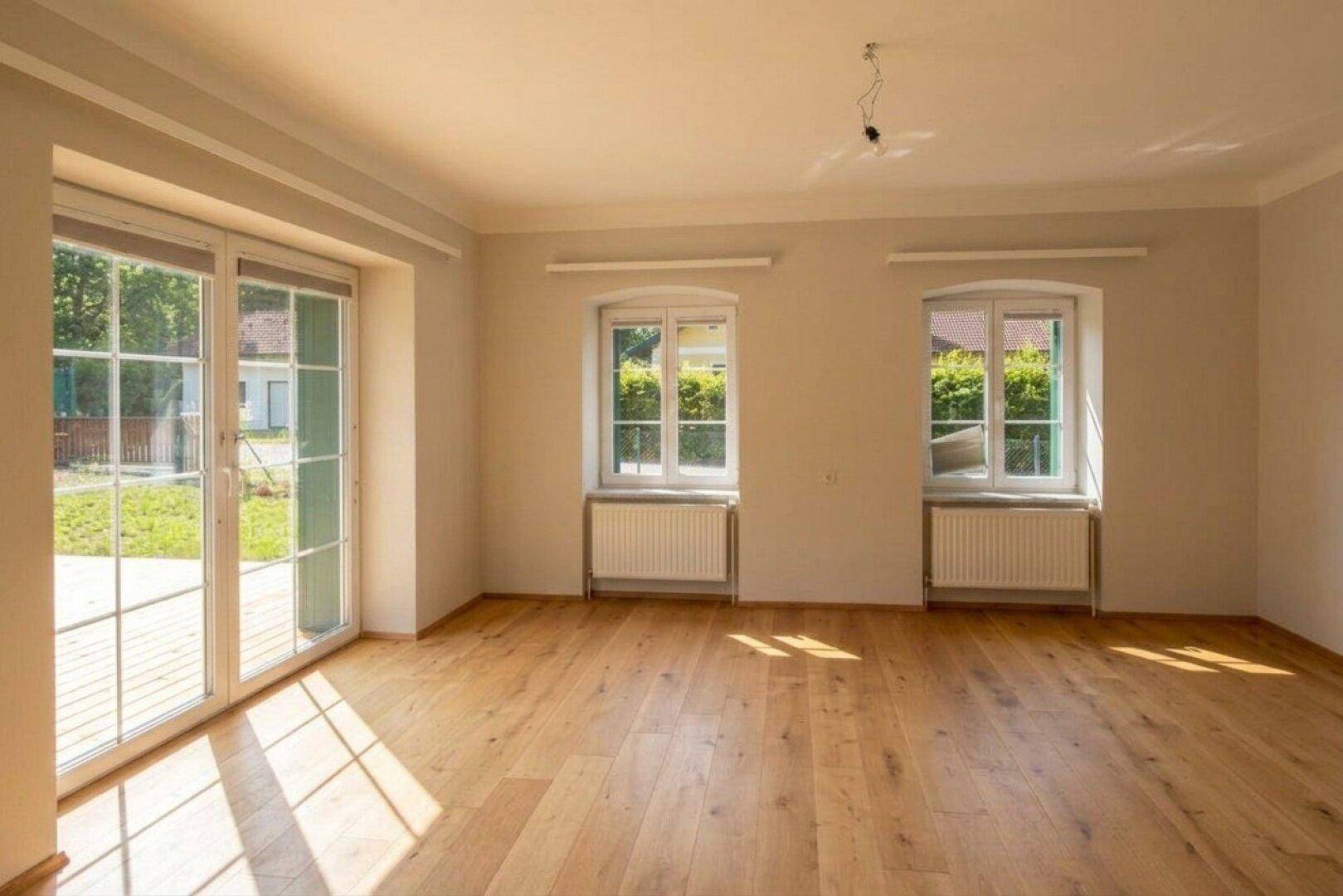 Heller, unmöblierter Wohnraum mit großen Fenstertüren und Eichenparkettboden, bietet Zugang zum Garten.