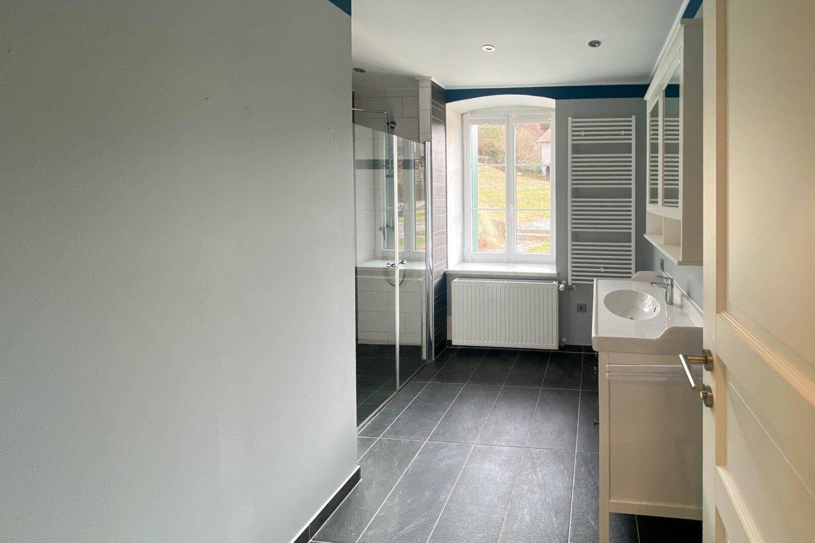 Modernes Badezimmer mit ebenerdiger Dusche, Einzelwaschbecken und Fenster mit Blick ins Grüne.