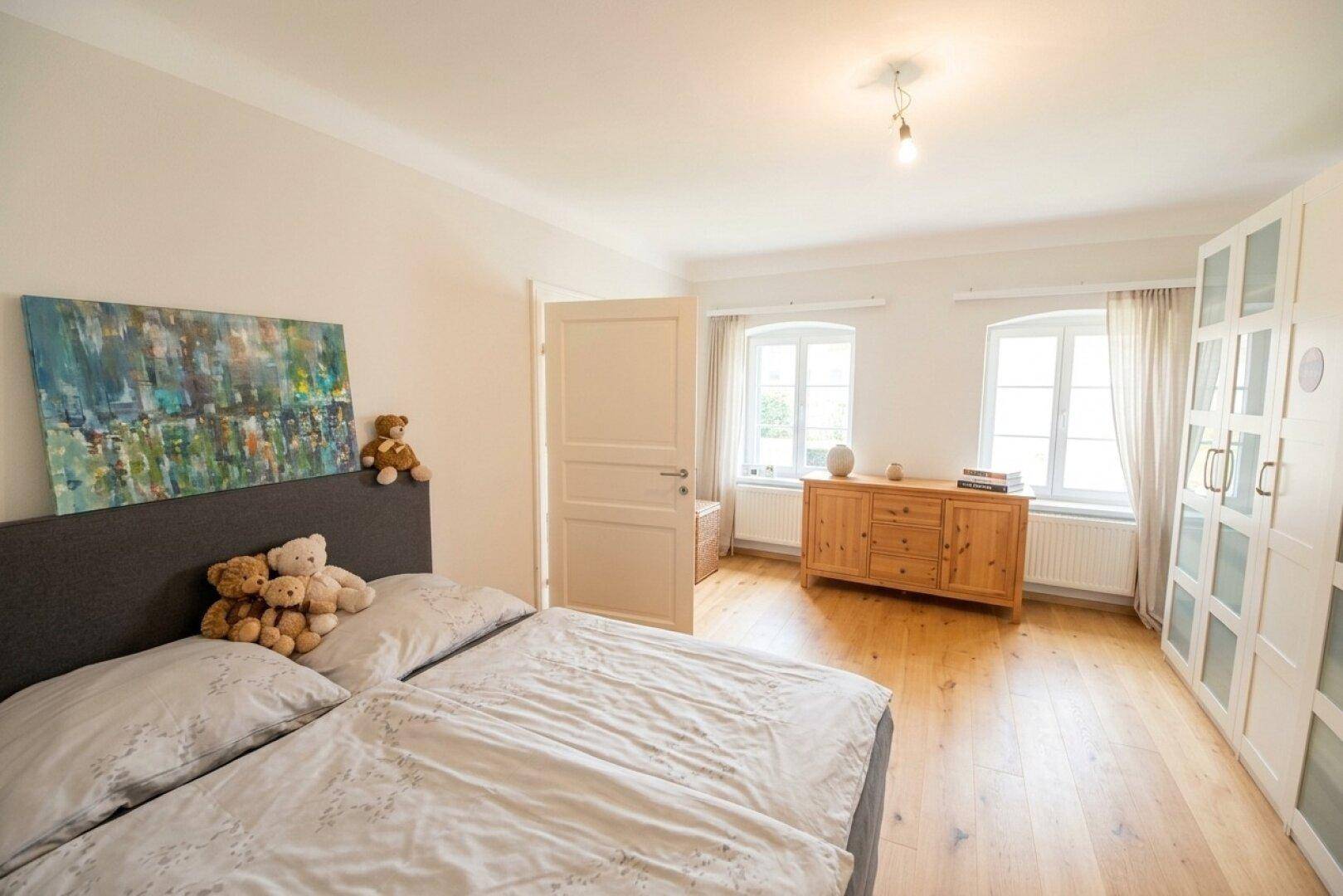 Helles Schlafzimmer mit Holzboden, Doppelbett und Einbauschränken, bietet viel Tageslicht.