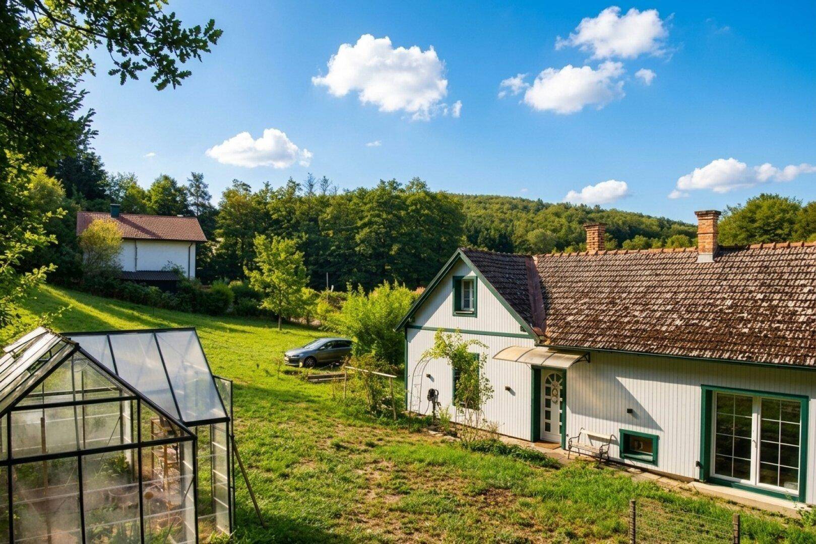 Weitläufiger Gartenbereich mit Gewächshaus und Blick auf das Landhaus in grüner Umgebung.