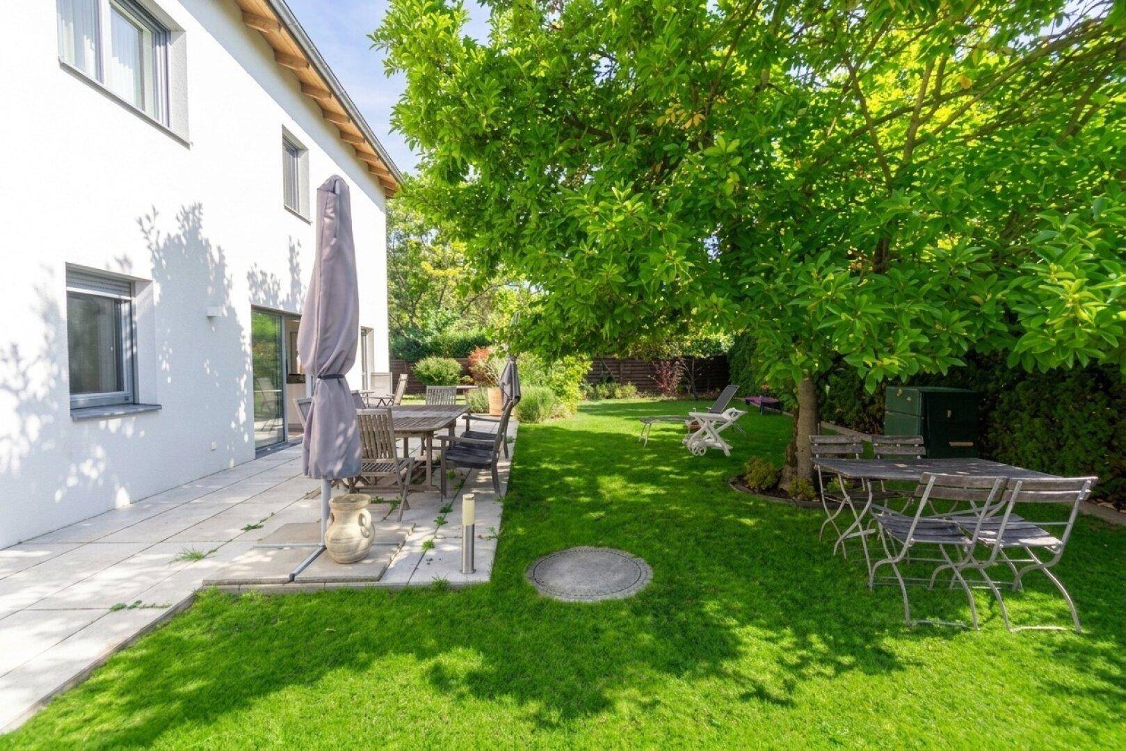 Großer Garten mit gepflasterter Terrasse, Sitzgelegenheiten und altem Baumbestand.