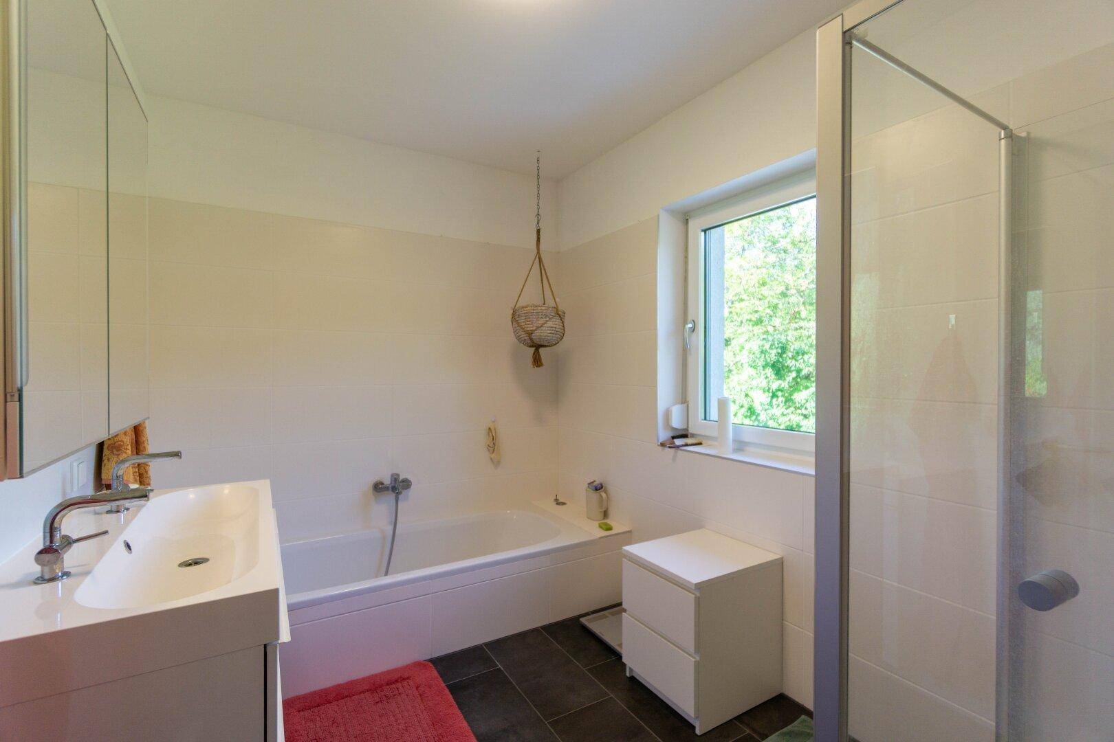 Helles Badezimmer mit Badewanne, separater Dusche und Fenster zum Garten.