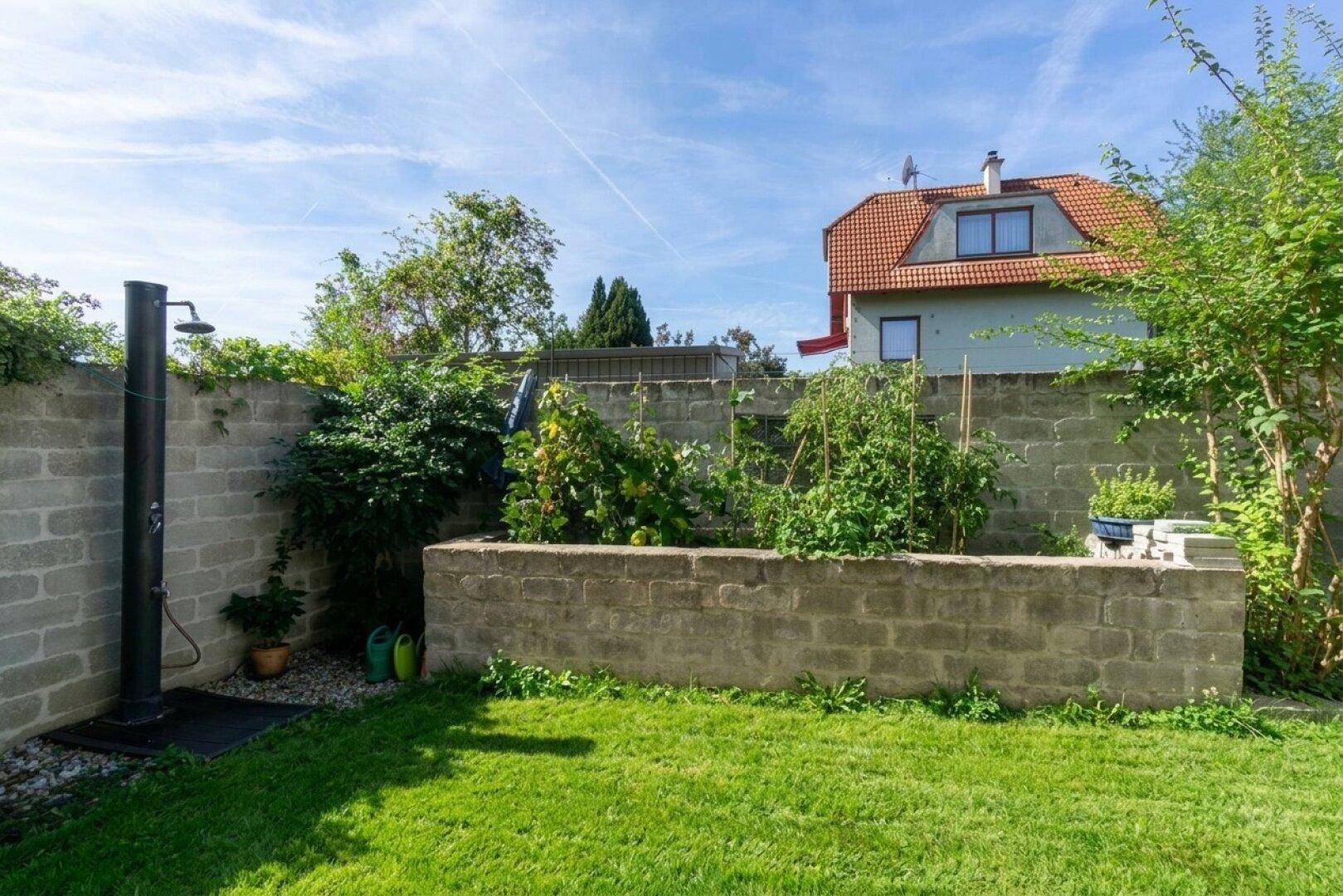 Gartenbereich mit Hochbeet, Außendusche und ummauertem Grundstück für Privatsphäre.
