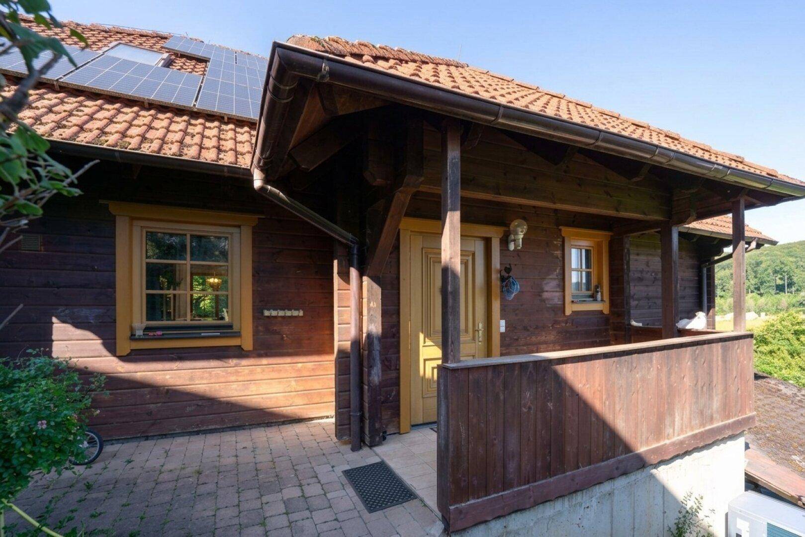 Eingangsbereich des Holzhauses mit überdachtem Vorbau und traditioneller Holzverkleidung unter einem Ziegeldach.