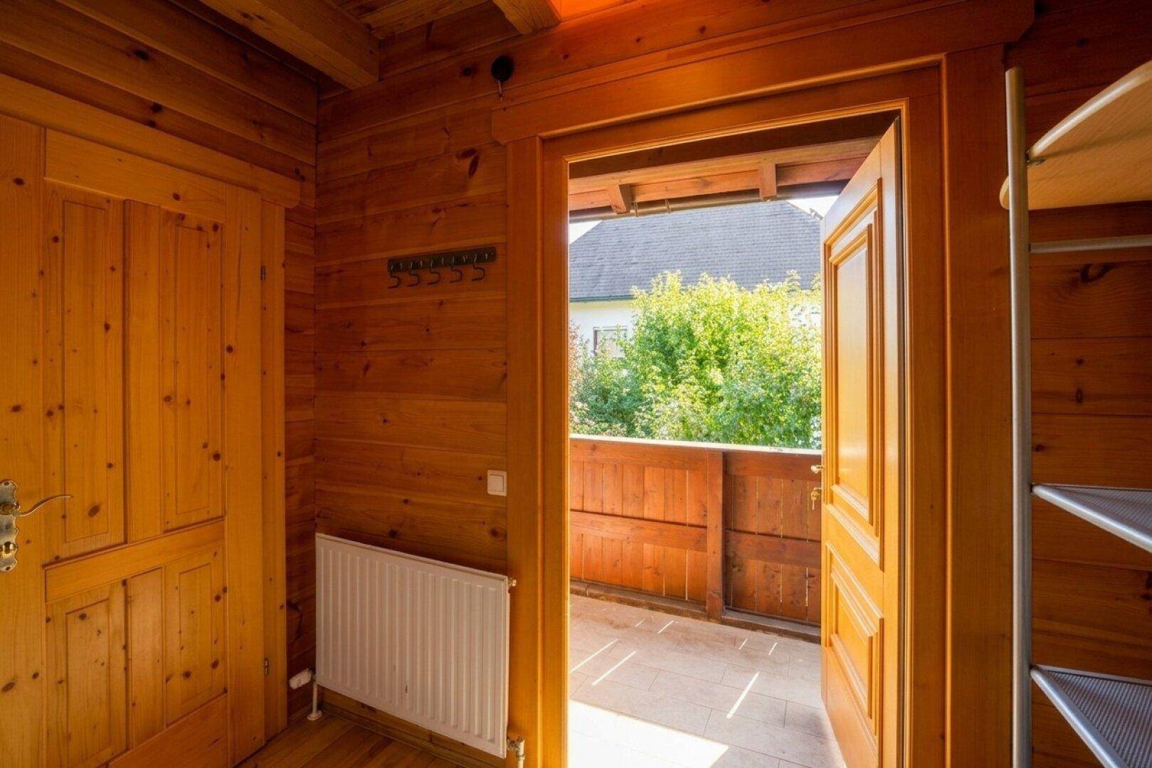 Heller Flur mit Holzverkleidung und Zugang zu einem kleinen Balkon mit Blick ins Grüne.
