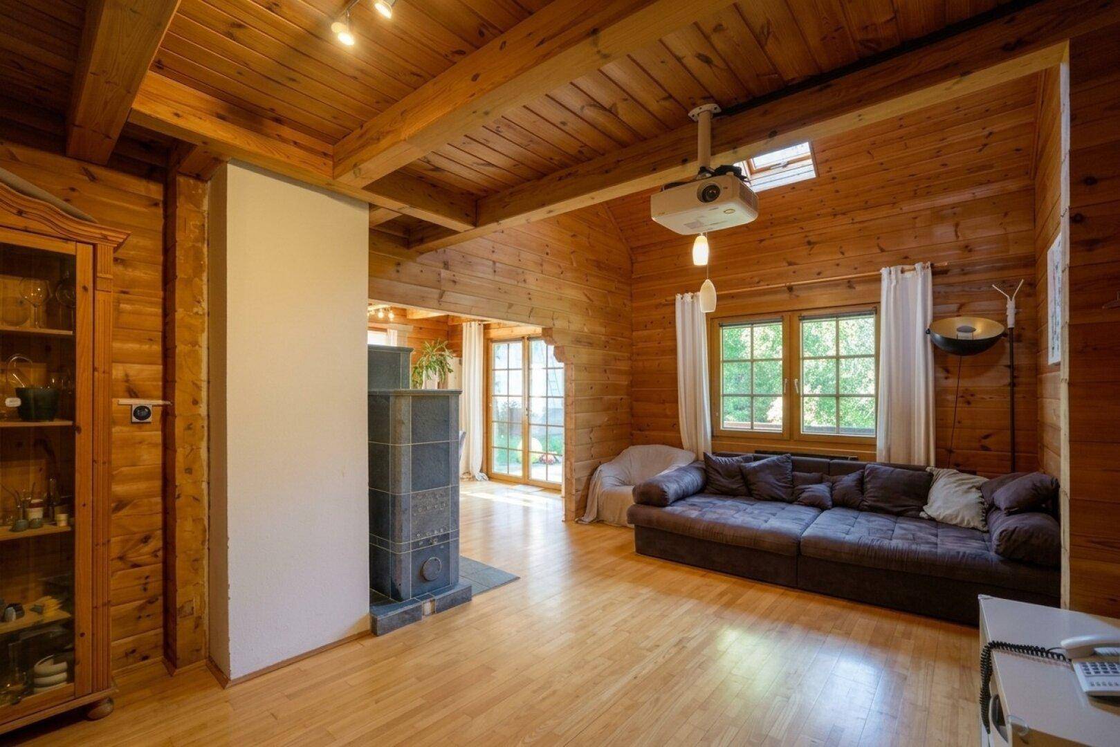 Geräumiges Wohnzimmer mit Holzbalkendecke, Kachelofen und großen Fenstern für viel Tageslicht.