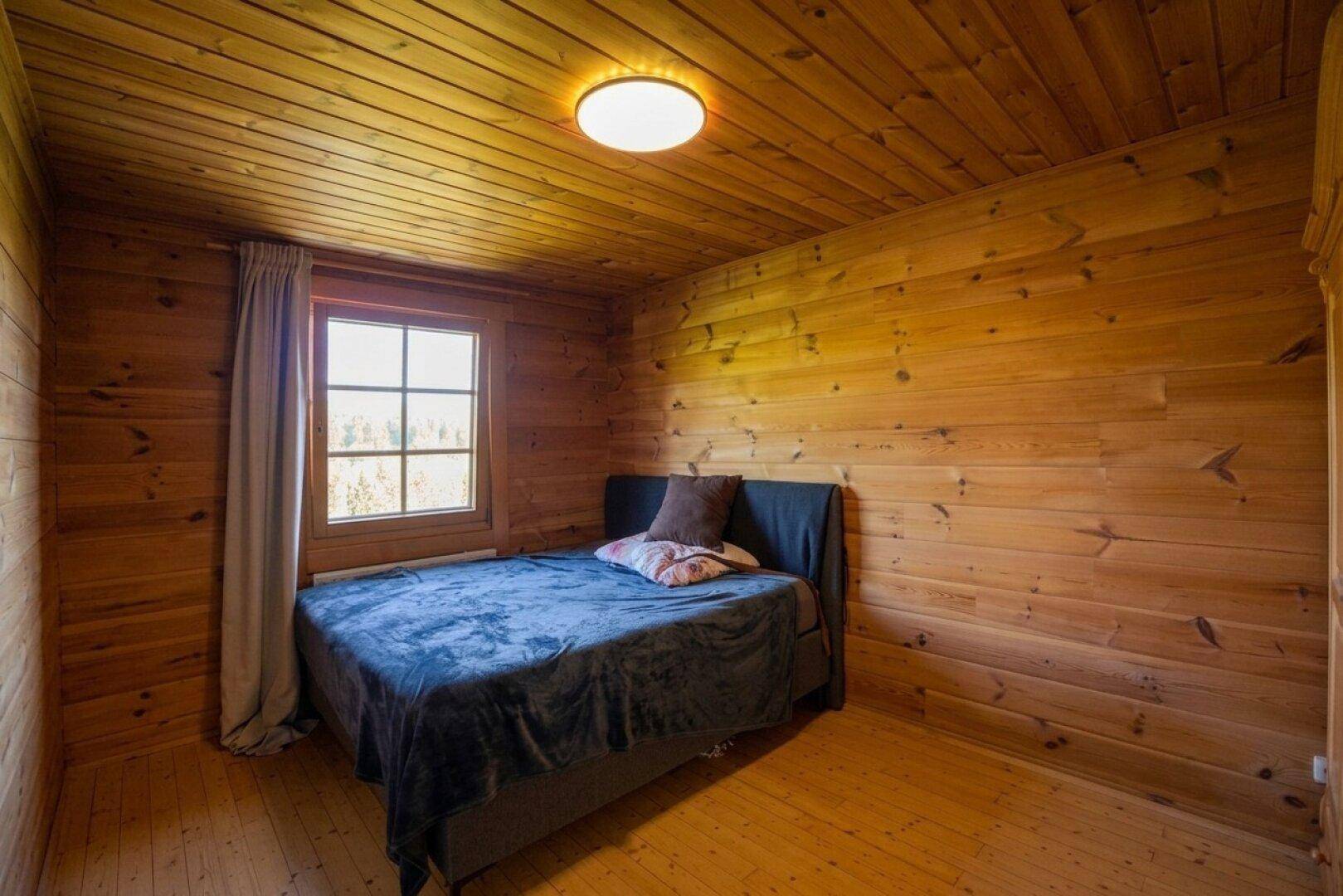 Schlafzimmer mit gemütlichem Bett, Holzverkleidung und Fenster mit Blick in die Natur.