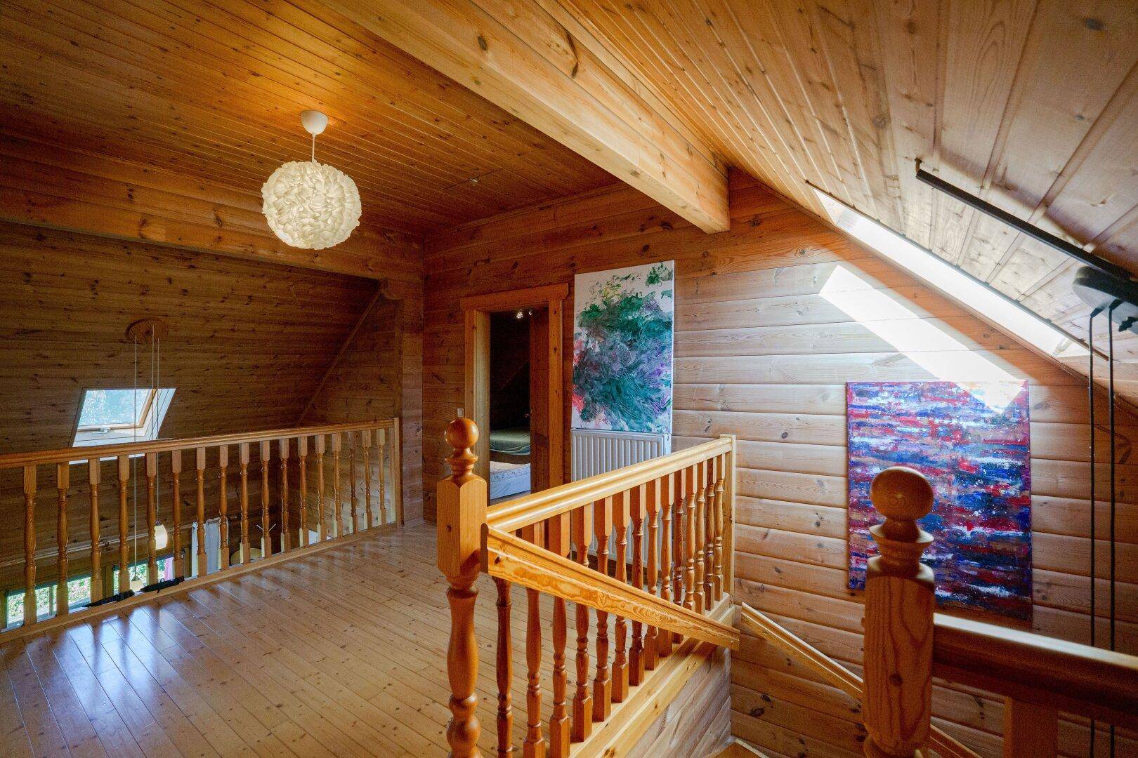 Heller Flur im Obergeschoss mit Holzgeländer, Holzboden und Dachfenstern für reichlich Tageslicht.