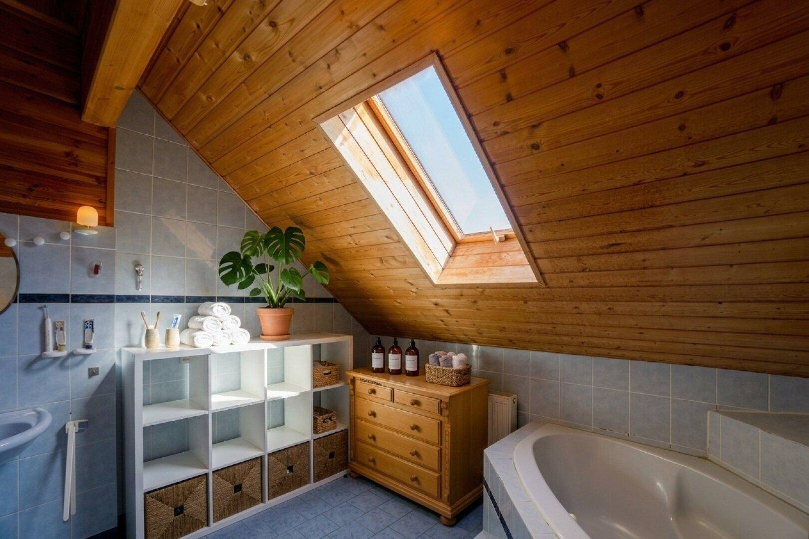 Badezimmer im Dachgeschoss mit Badewanne, Dachfenster und Holzdecke für eine helle Atmosphäre.