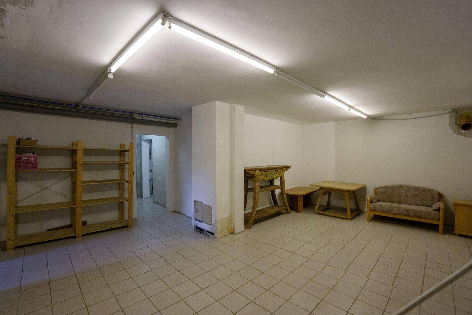 Geräumiger Kellerraum mit Fliesenboden, einfacher Beleuchtung und praktischen Stauraummöglichkeiten.