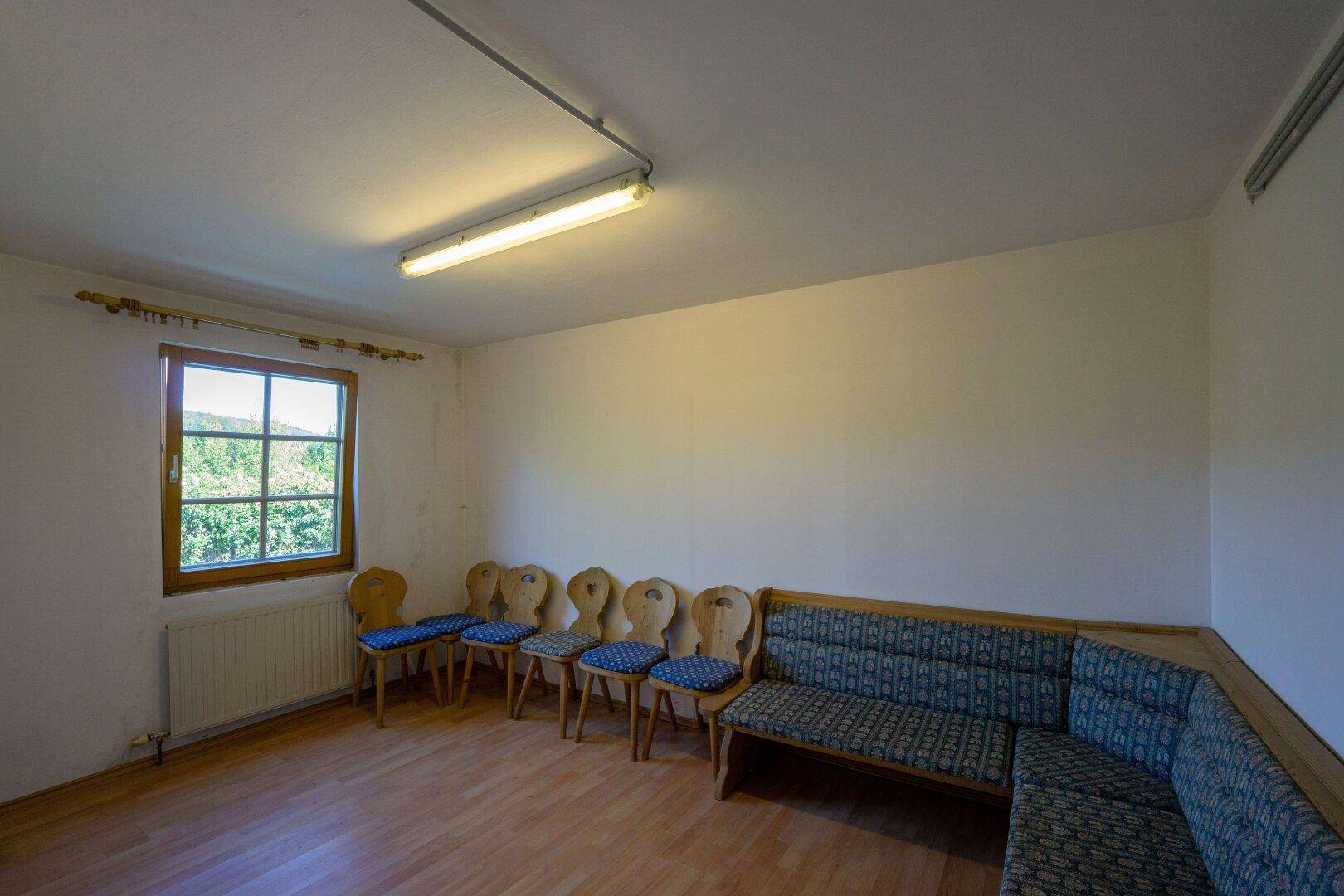 Kellerraum mit Fenster, Holzboden und traditioneller Sitzgelegenheit, ideal als Hobbyraum nutzbar.
