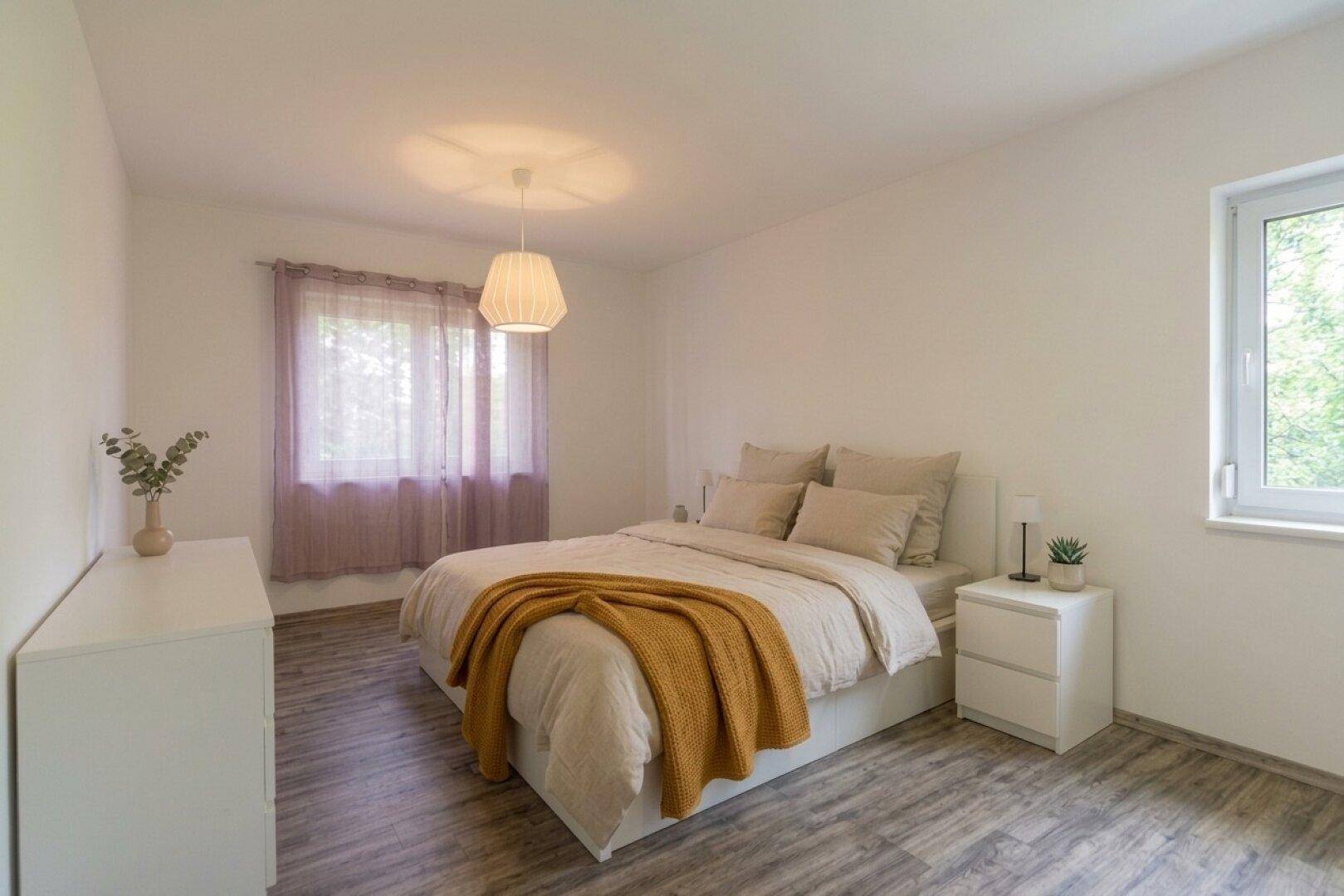 Gemütliches Schlafzimmer mit Doppelbett, Nachttischen und Fenster mit Vorhängen.