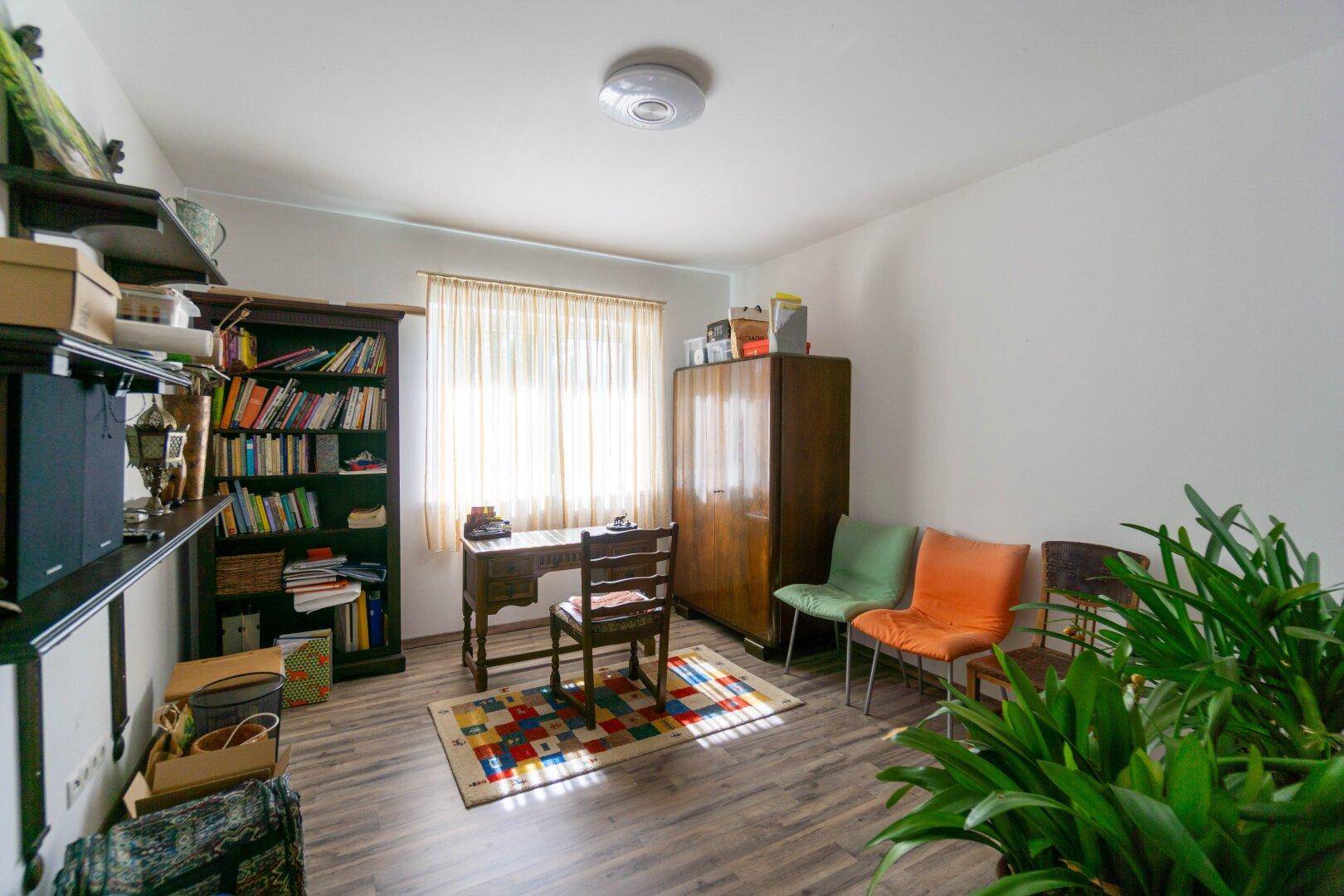 Funktionales Arbeitszimmer mit Schreibtisch, Bücherregal und bunten Stühlen.