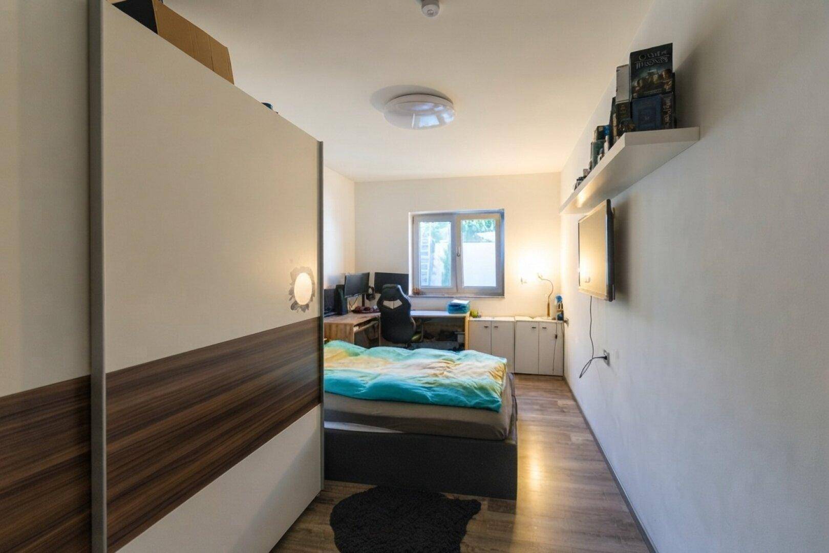 Gemütliches Schlafzimmer mit Holzboden, Schreibtisch und Fenster mit Blick ins Grüne.