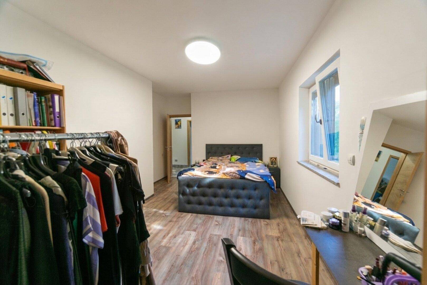 Helles Schlafzimmer mit Holzboden, großem Bett und offenem Kleiderständer.