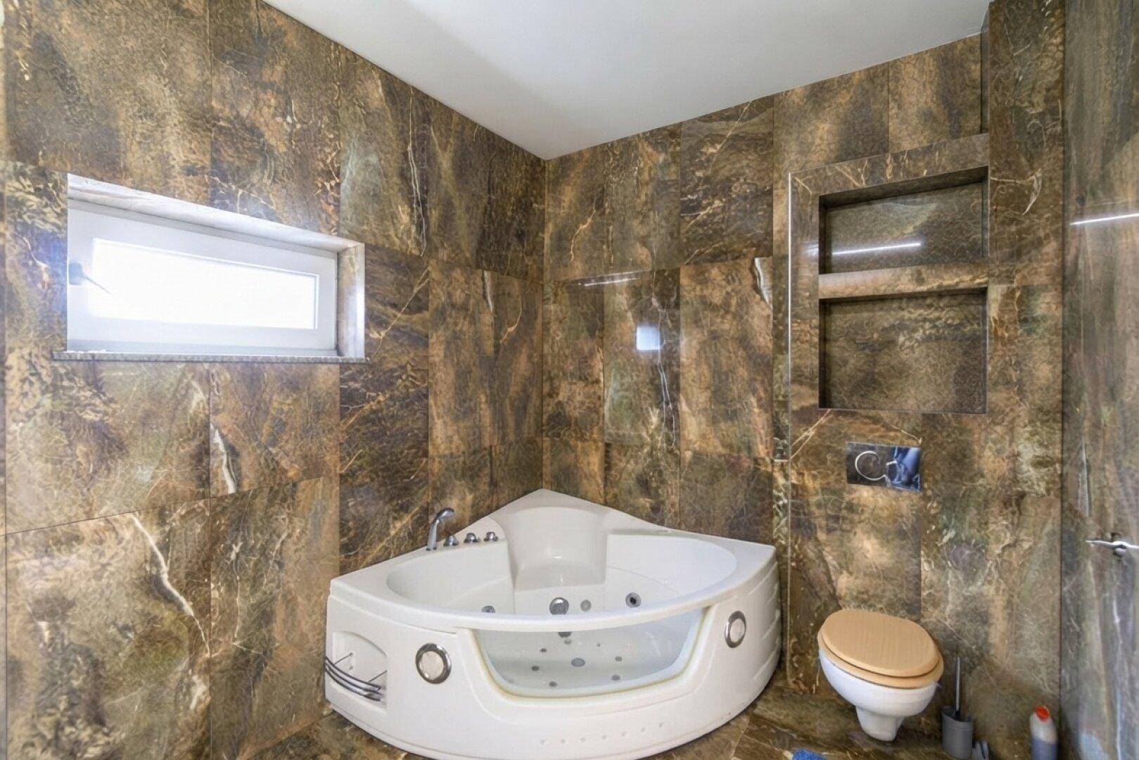 Luxuriöses Badezimmer mit braunen Marmorfliesen, Eckbadewanne und Wand-WC.