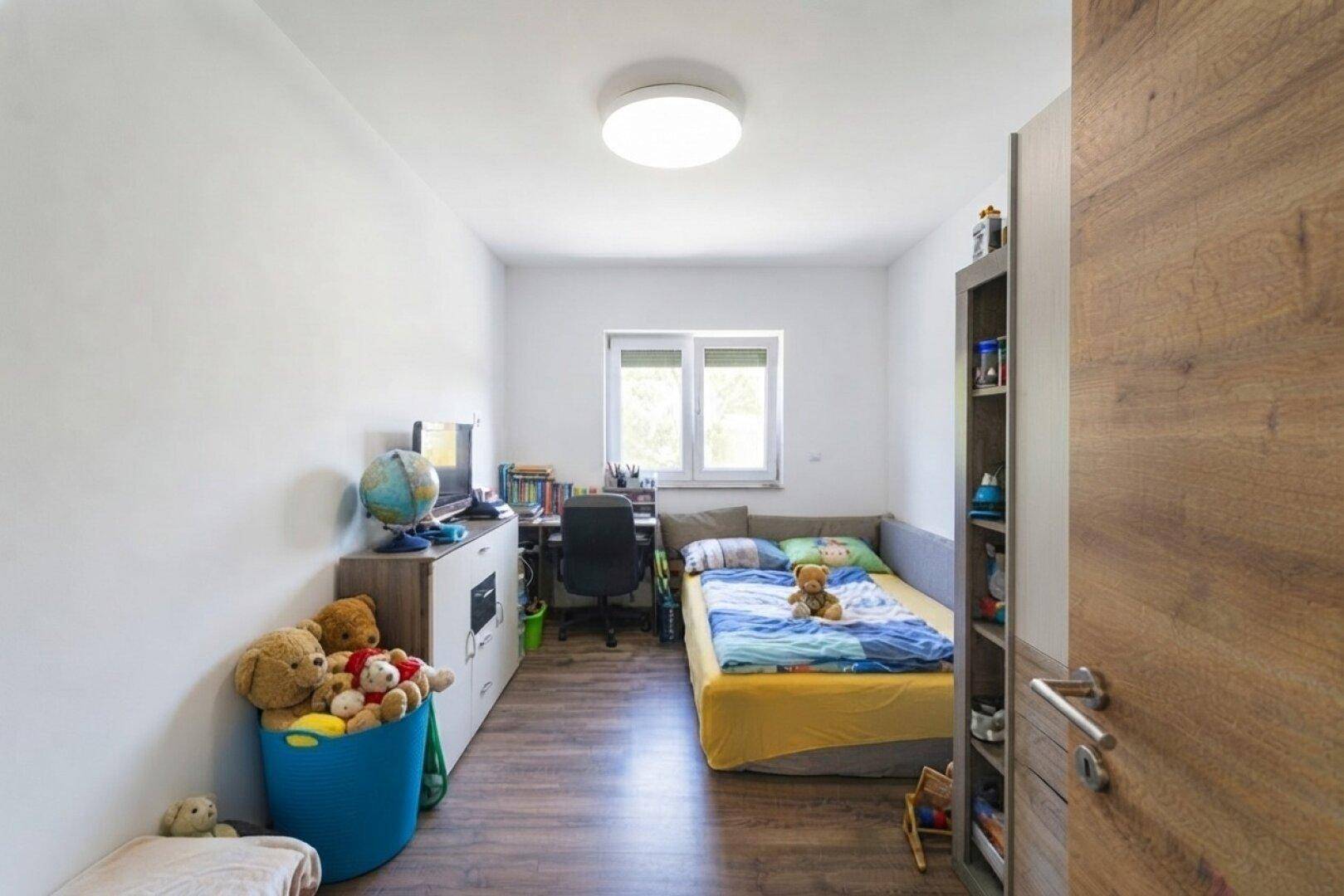 Kinderzimmer mit Holzboden, Einzelbett, Schreibtisch und Spielzeug in freundlichen Farben.