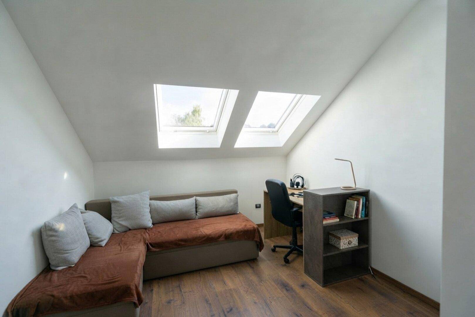 Dachgeschosszimmer mit Schreibtisch, Sofa und zwei Dachfenstern für viel Tageslicht.